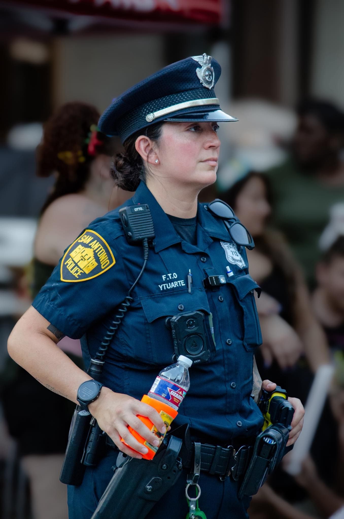 San Antonio police officer in blue uniform holding water bottle at outdoor public event.