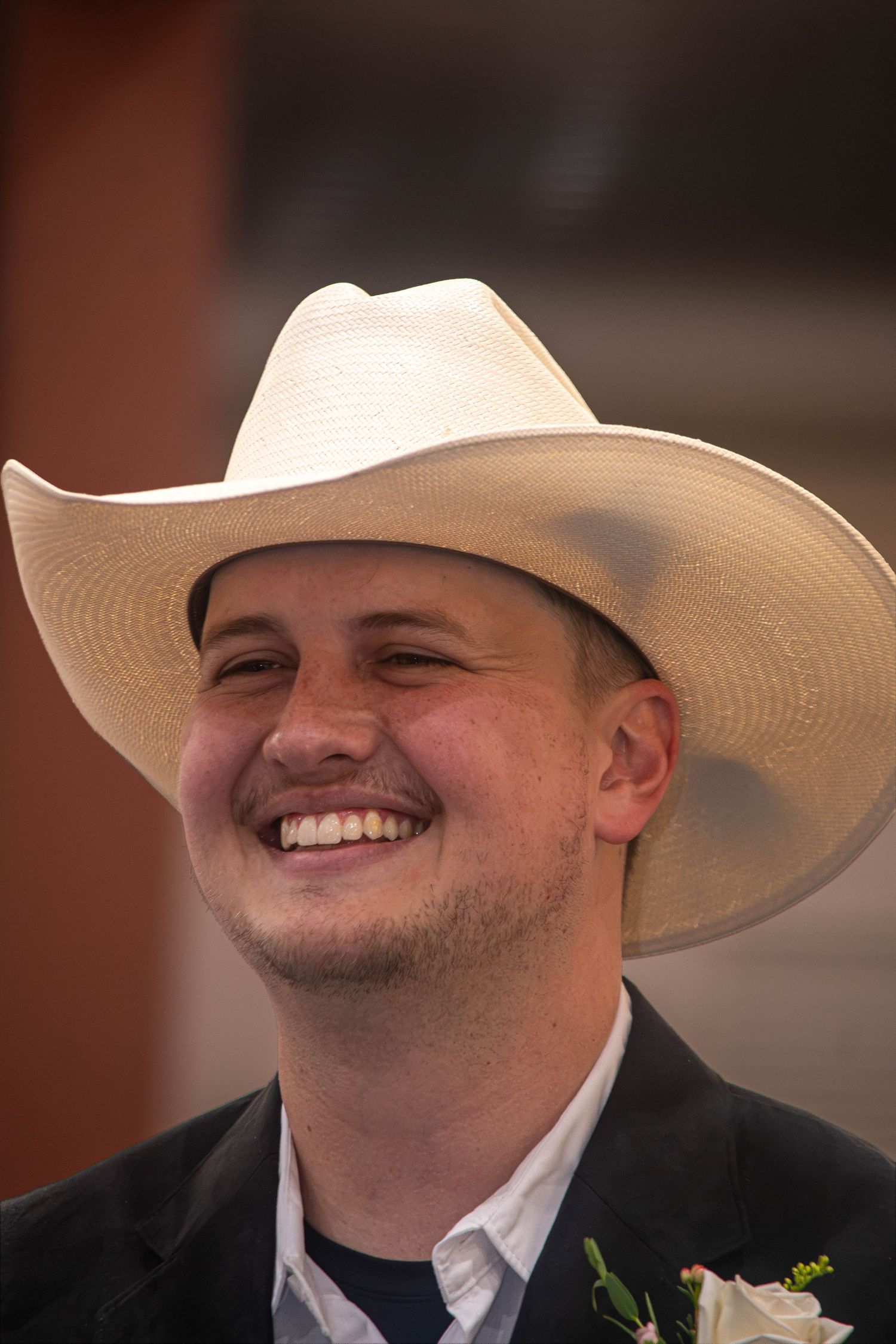 Happy groom smiling in white cowboy hat and black suit with boutonniere.