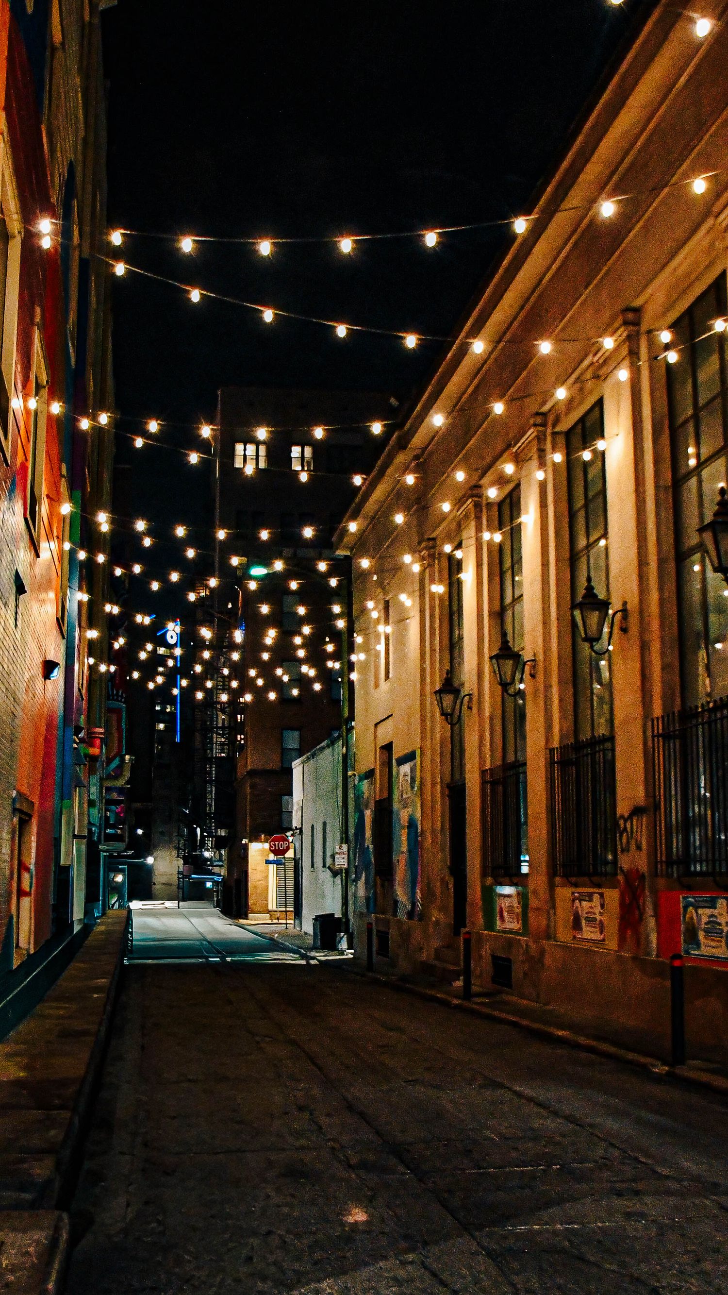 Narrow urban alley at night decorated with warm string lights strung between historic stone buildings.