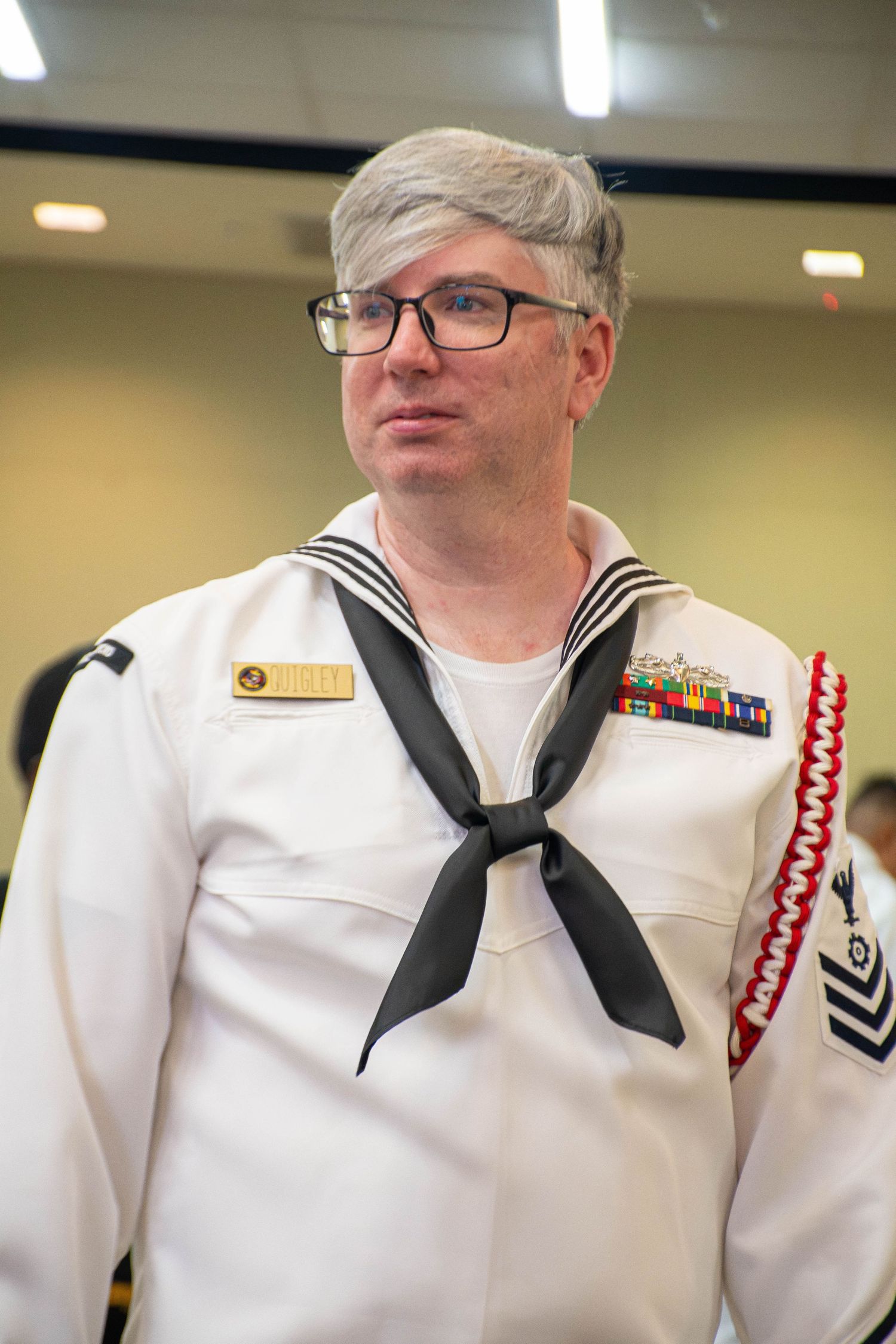Senior Navy petty officer in dress whites with service ribbons stands at military ceremony.