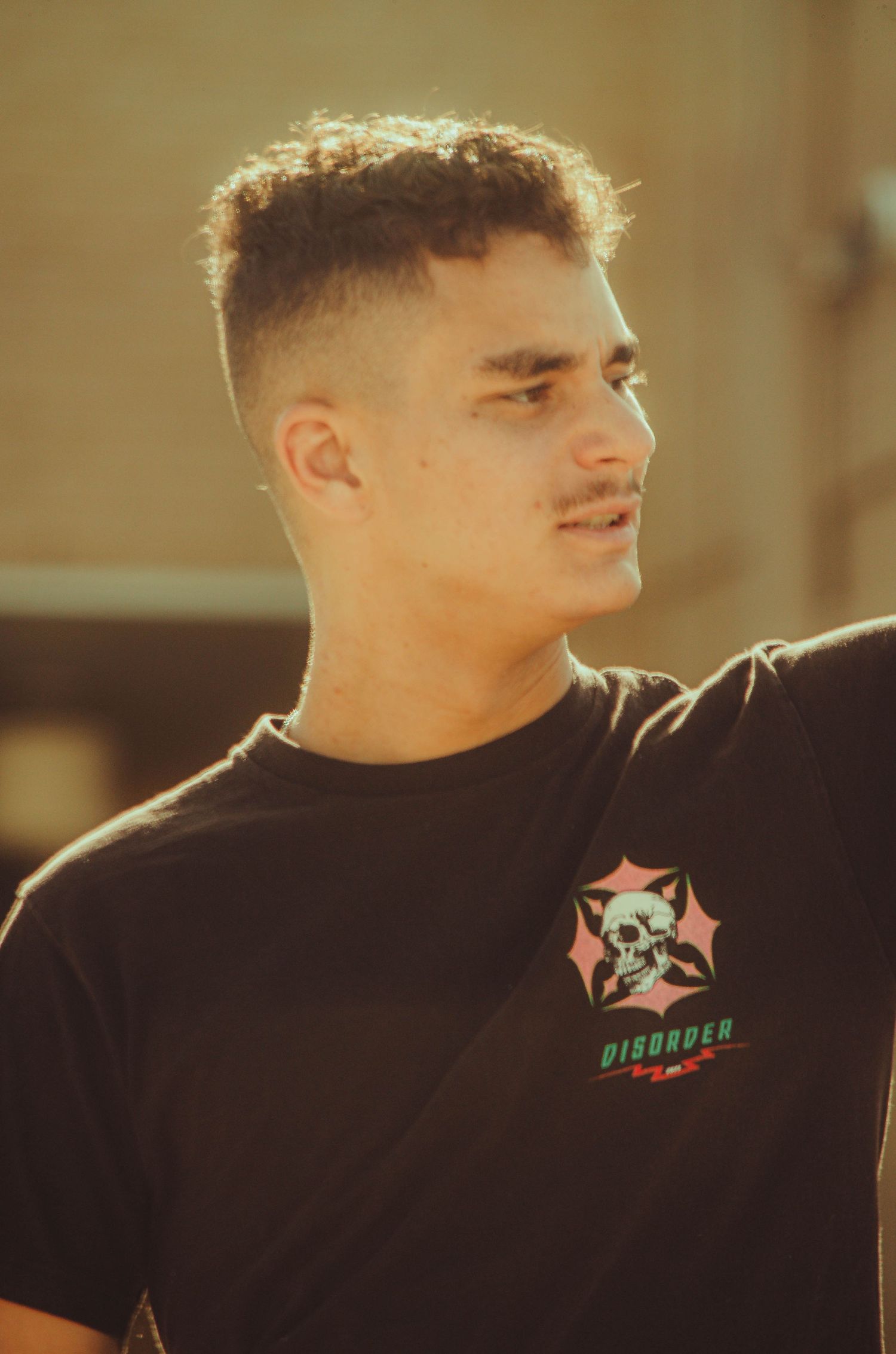 Young man with a fade haircut wearing a black Disorder graphic t-shirt photographed in warm sunlight.