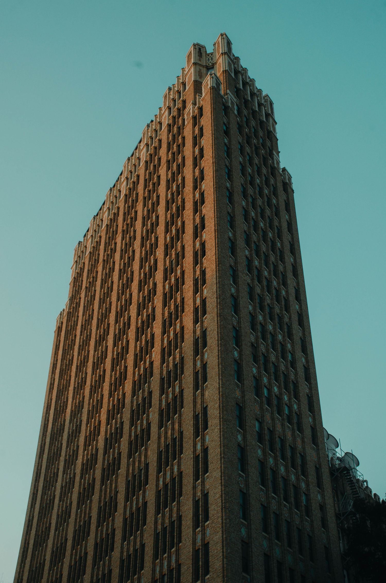Art Deco brick skyscraper rising against a clear teal sky at sunset.