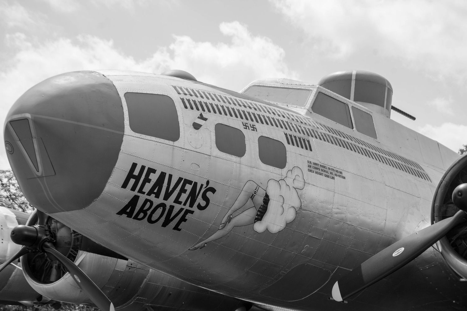 Black and white photo of a B-17 bomber nose art reading Heaven's Above with propellers visible.