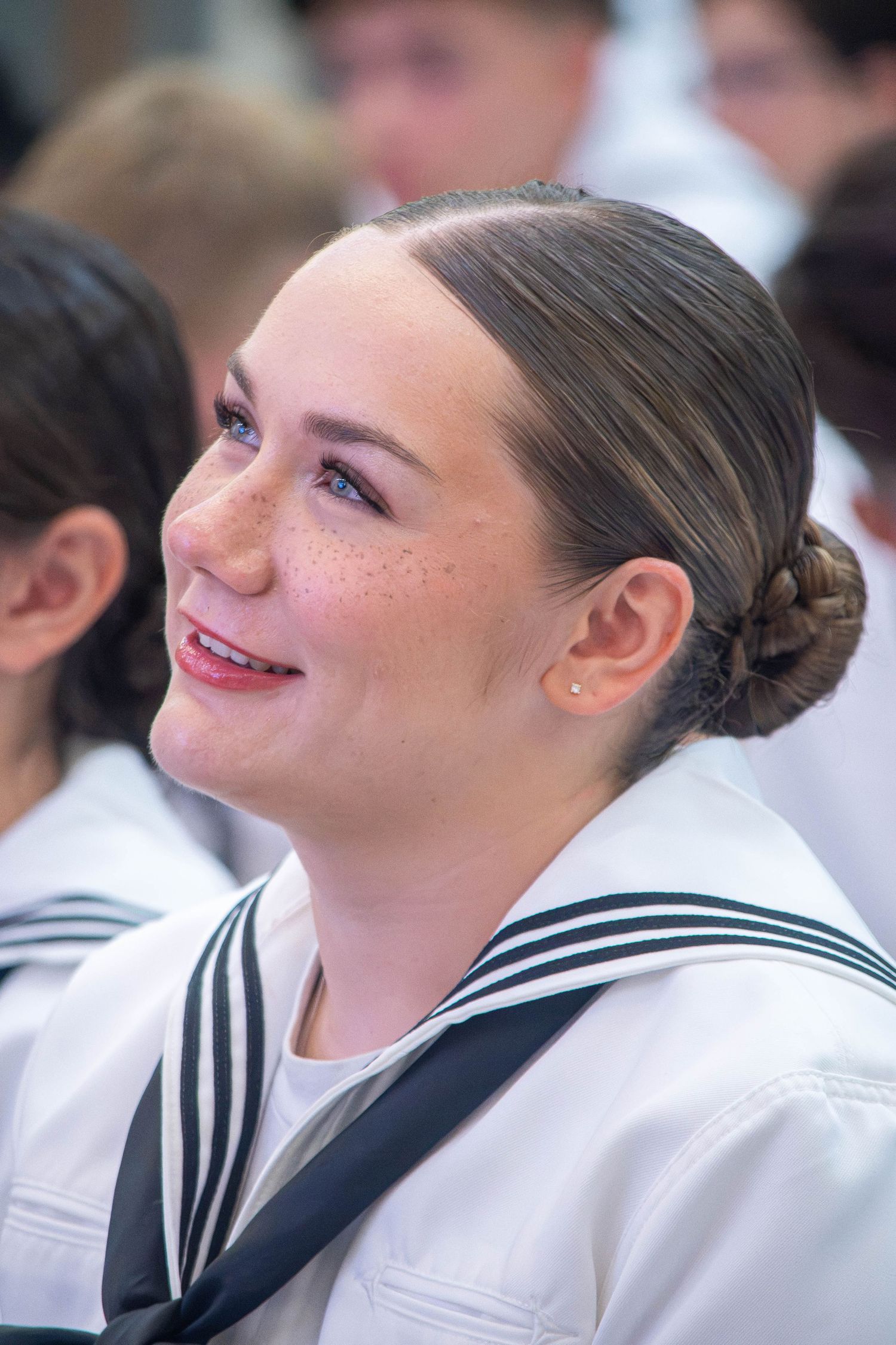 Smiling young female US Navy sailor with freckles and braided hair in white uniform.