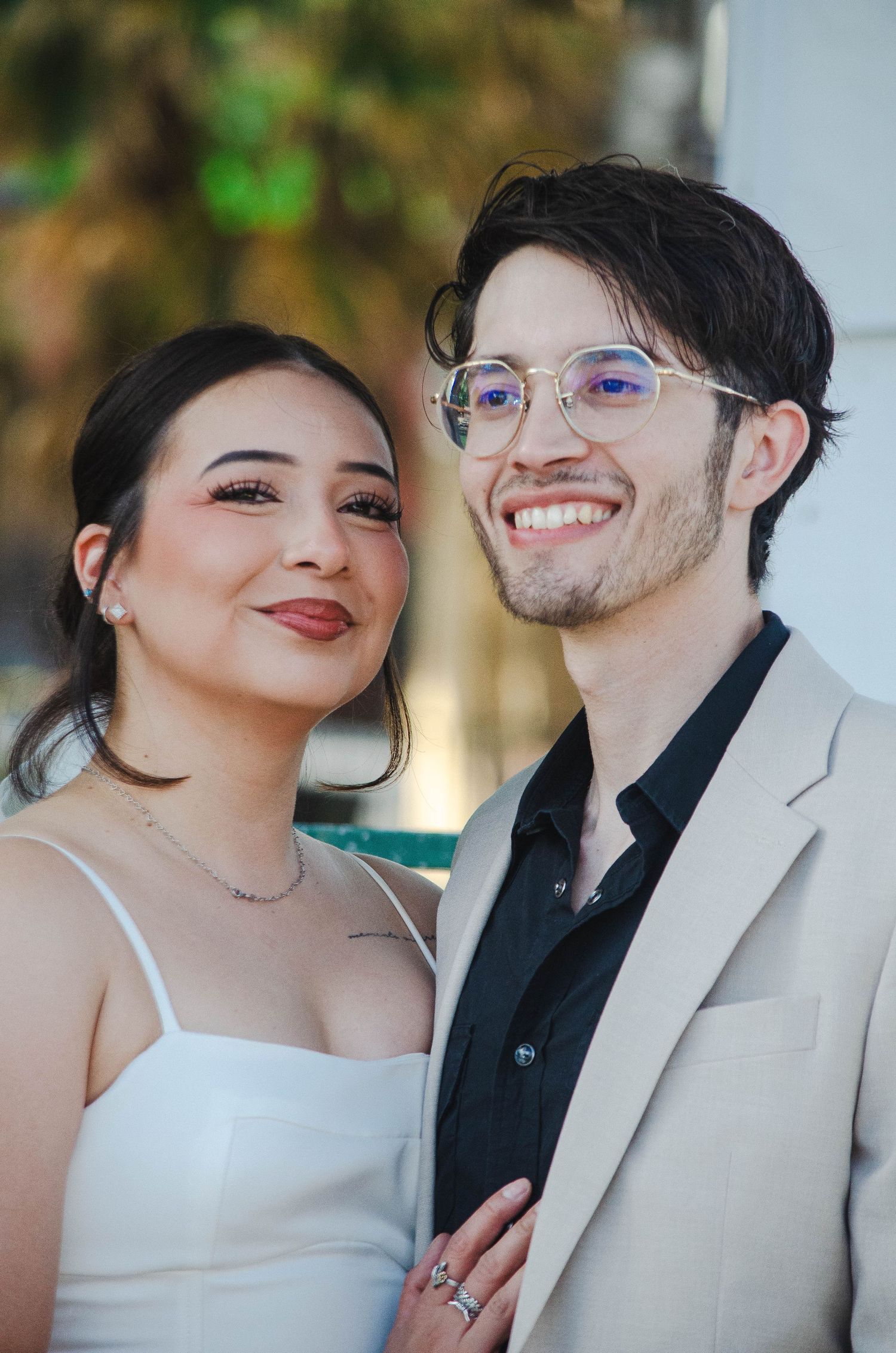 Close-up portrait of smiling bride and groom, groom wearing glasses and beige suit on their wedding day.