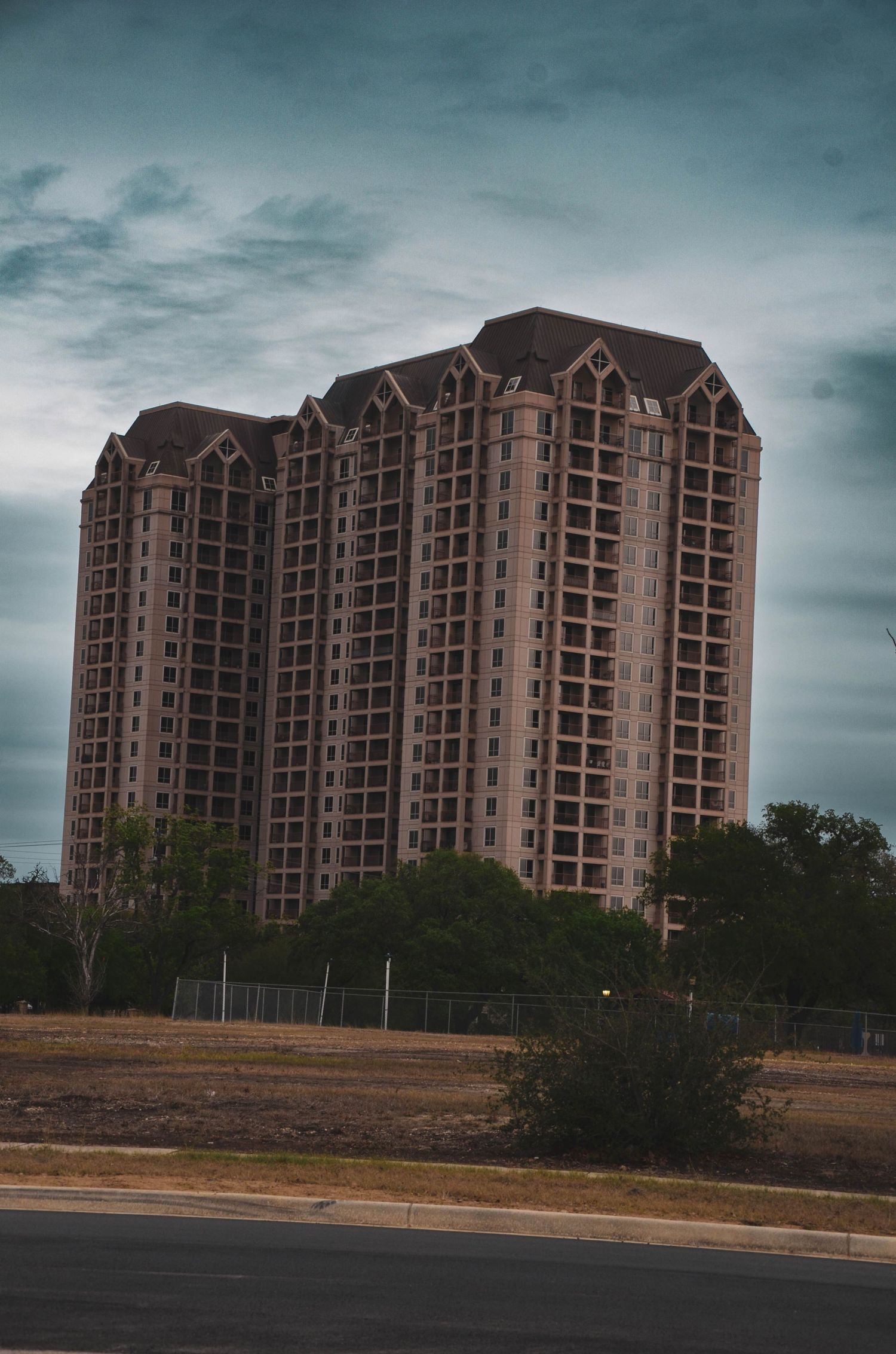 Tall multi-story residential condominium building with Gothic-style roofline under a cloudy sky.