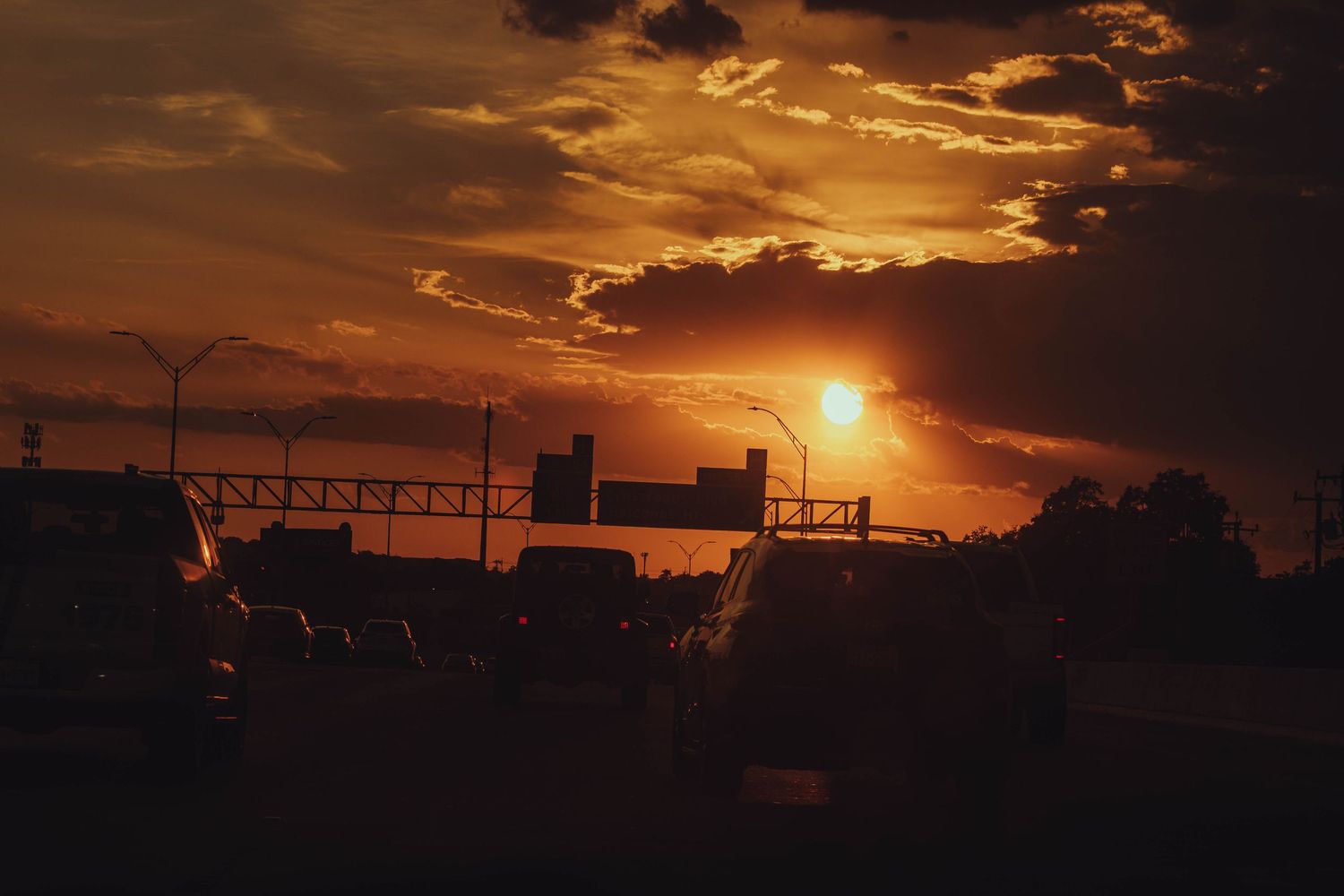 Dramatic orange sunset silhouettes highway traffic and overpass against glowing cloudy sky.