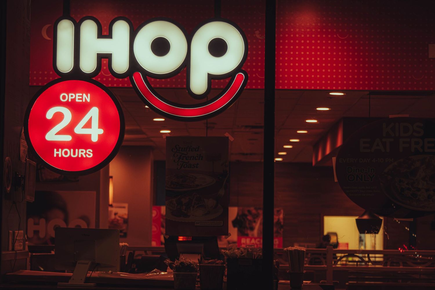 IHOP restaurant exterior at night with illuminated red sign and Open 24 Hours circular logo on window.