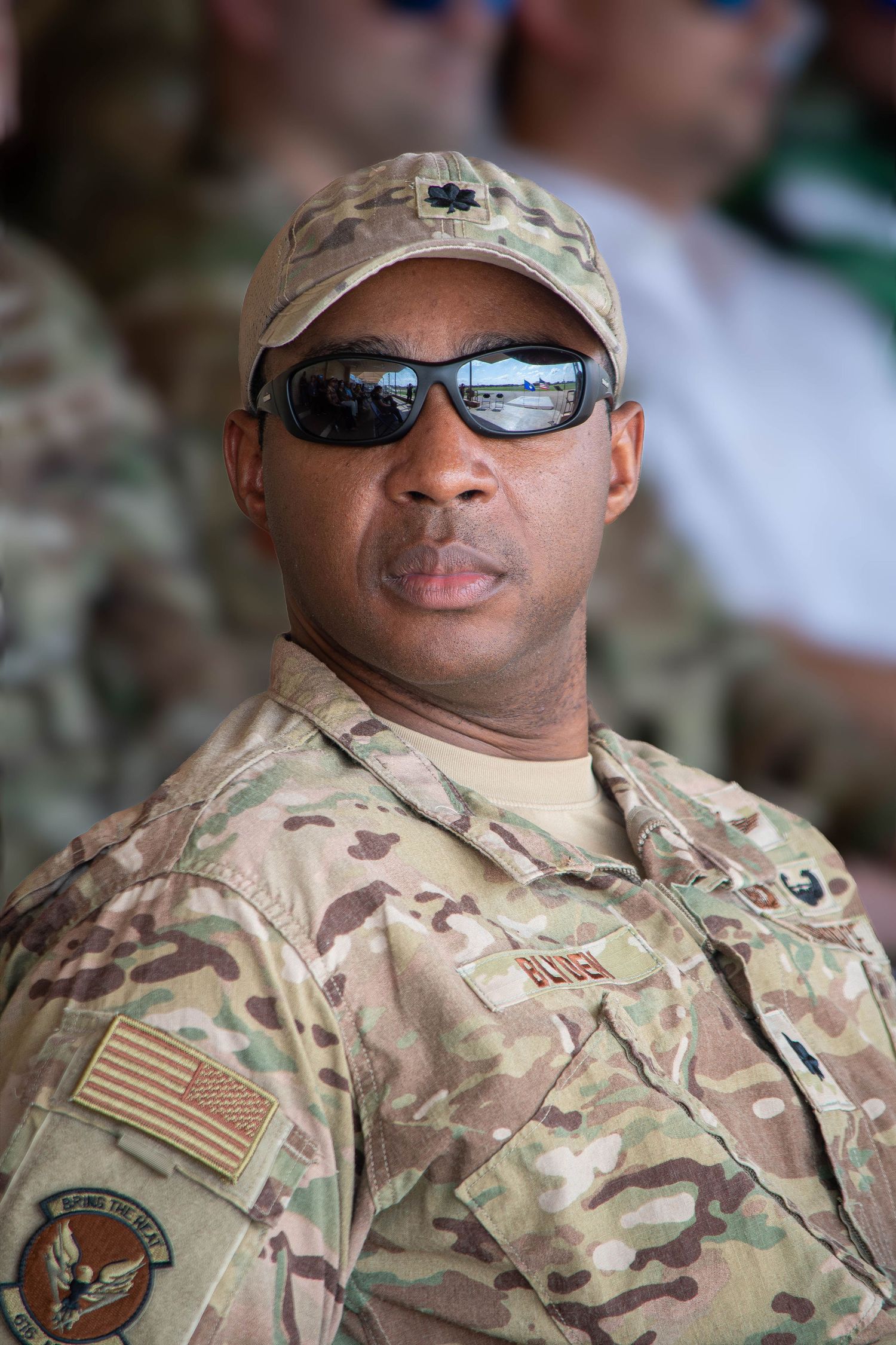 A US Air Force airman in camouflage uniform and reflective sunglasses at an outdoor event.