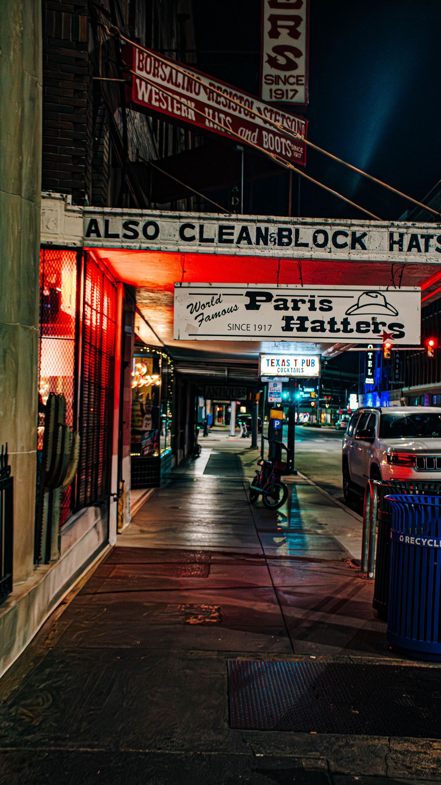 Paris Hatters historic hat shop storefront on a wet San Antonio sidewalk illuminated at night since 1917.