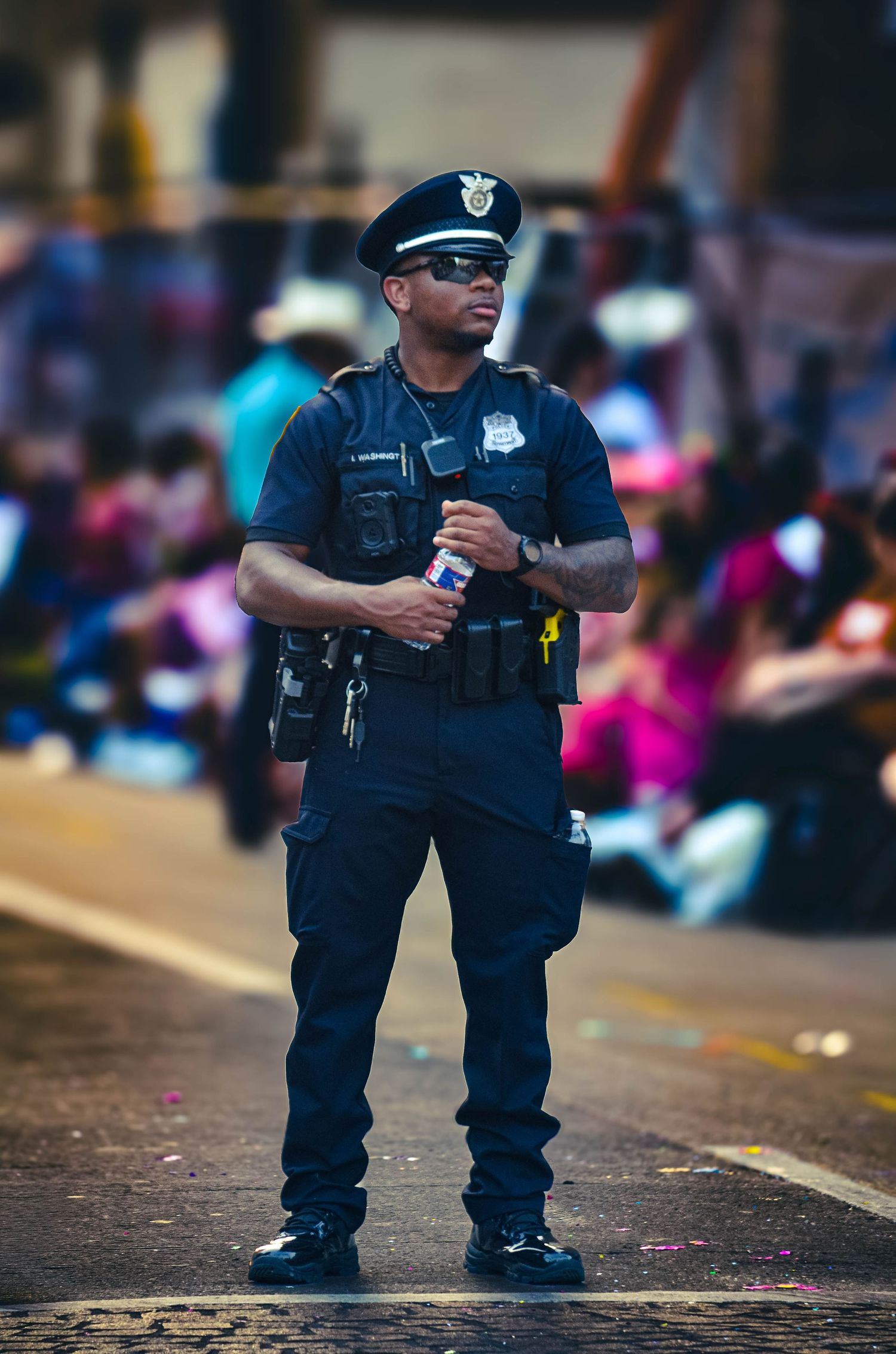 Black male police officer in blue uniform standing on parade route holding radio.