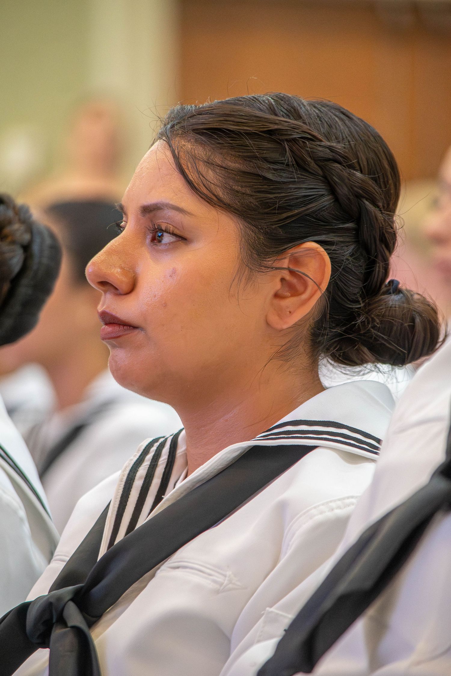 Female Navy sailor with braided updo hairstyle in white uniform attending a military ceremony.