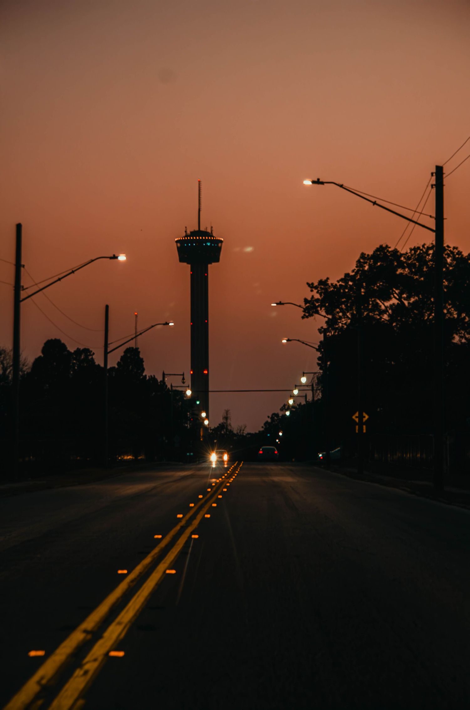 Silhouetted road at sunset with Tower of the Americas and glowing street lights in San Antonio.