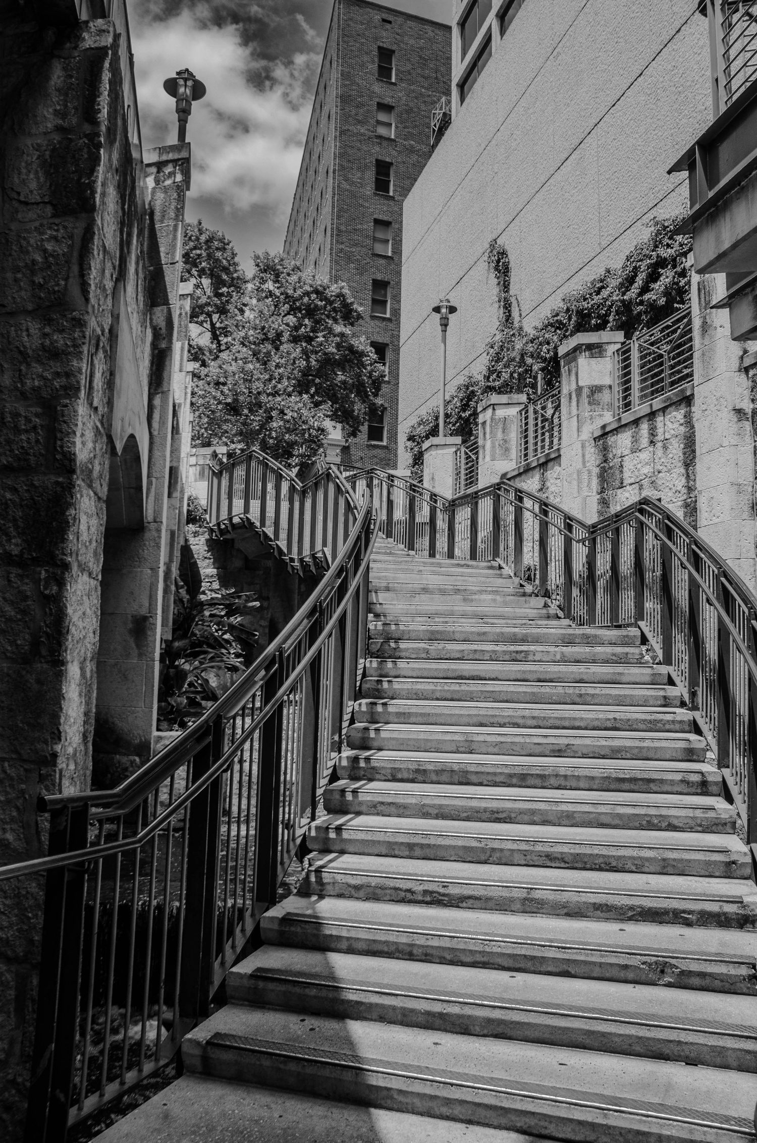 Black and white urban staircase with iron railings leading upward between historic stone buildings.