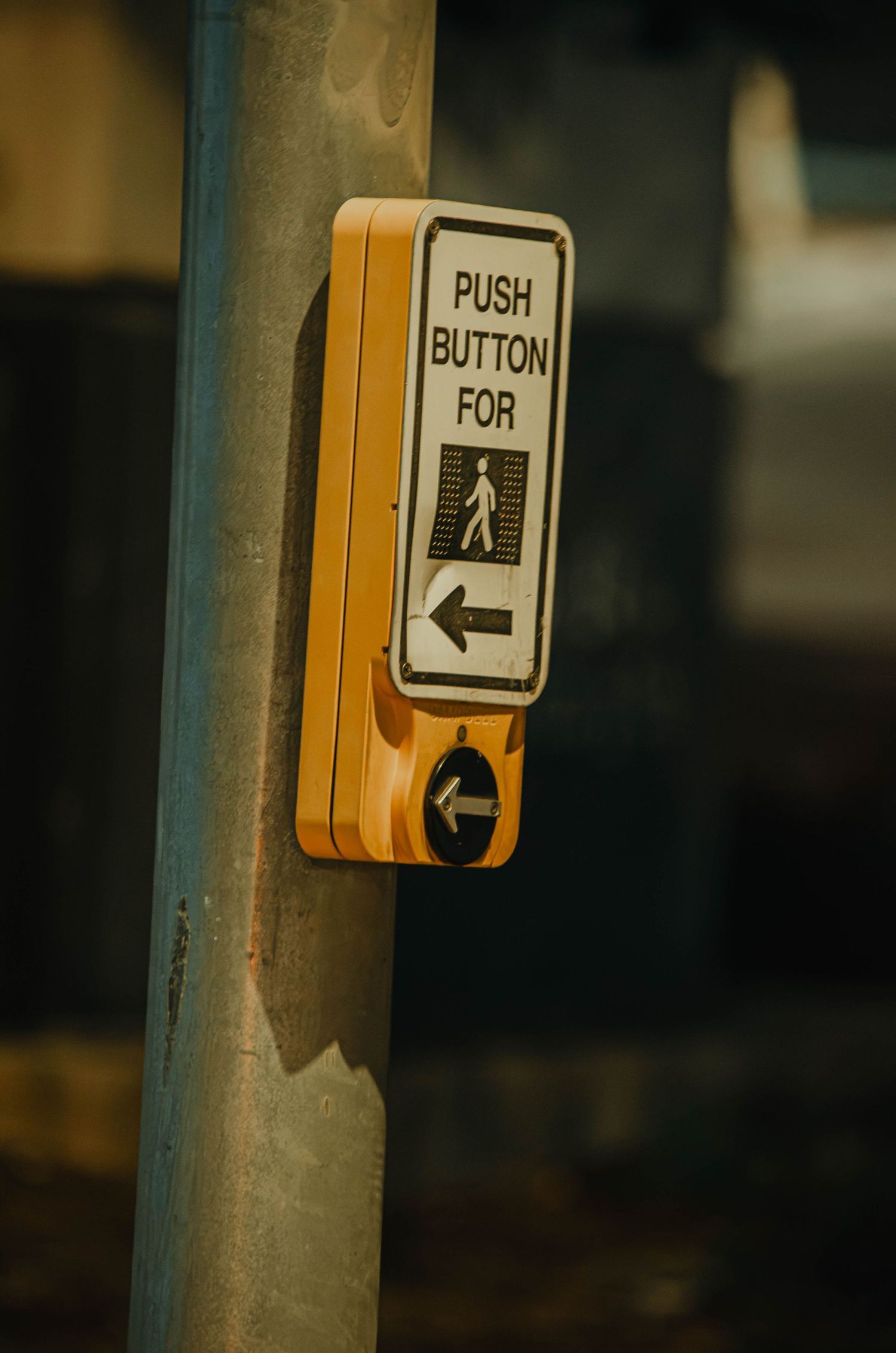 Yellow pedestrian crosswalk push button mounted on a metal pole.
