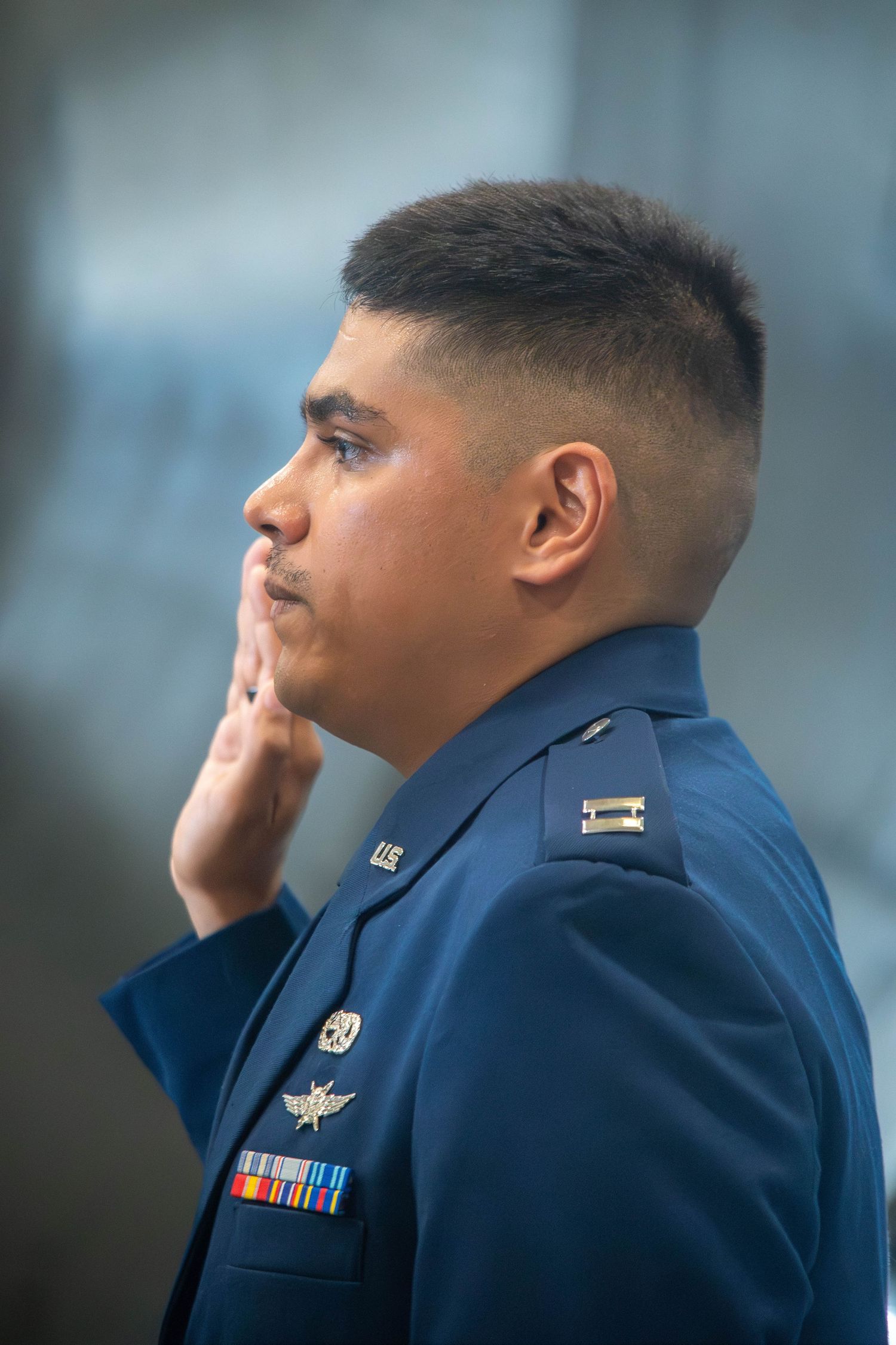 US Air Force officer in dress blue uniform with medals standing at attention in profile view.