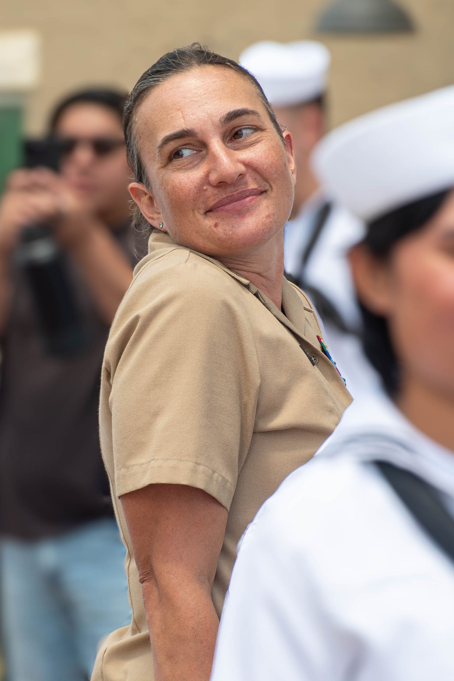 Female Navy officer in tan uniform smiling during an outdoor military ceremony.