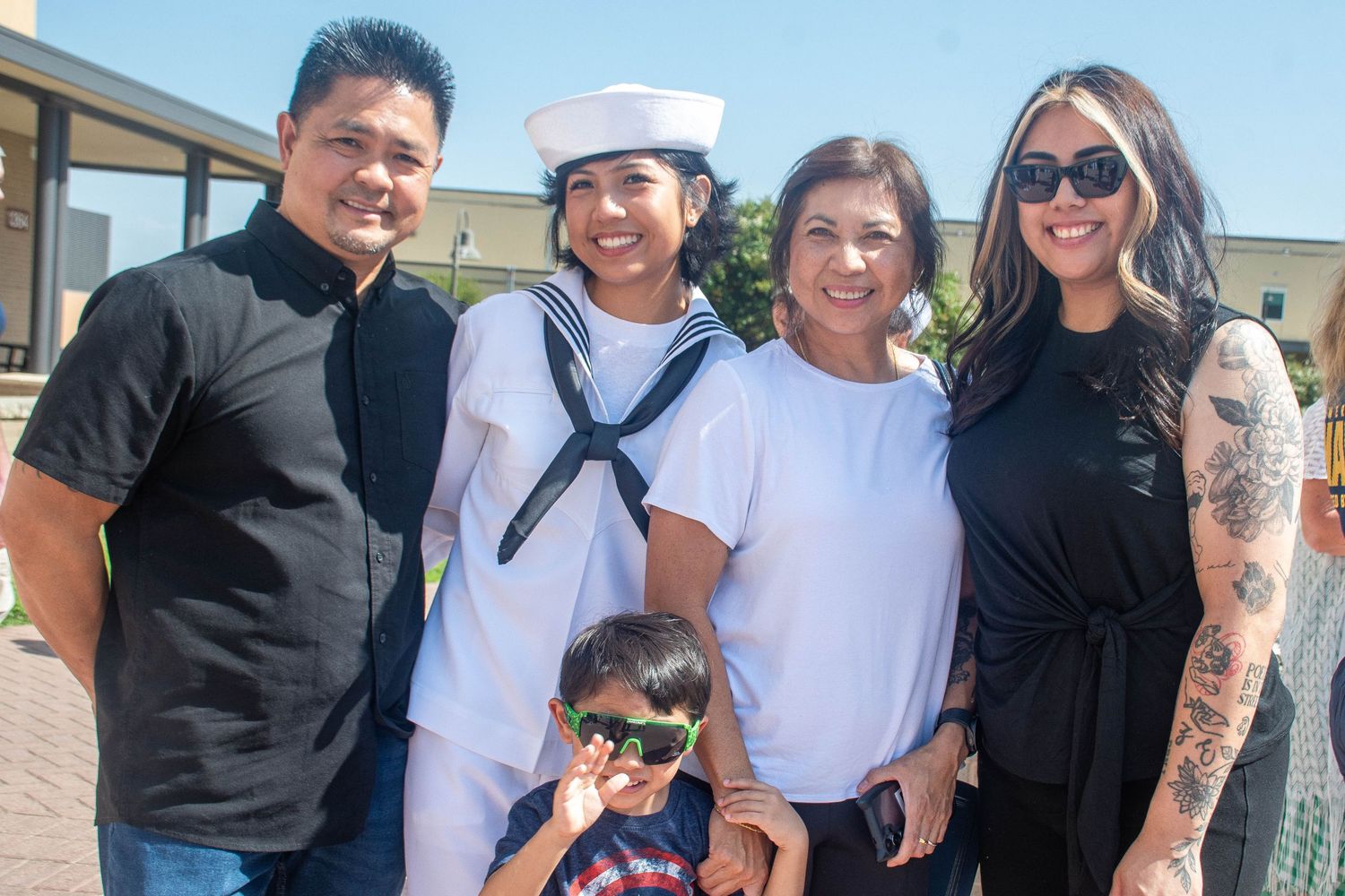 Navy sailor in dress whites poses with family of five including young child at military graduation ceremony.