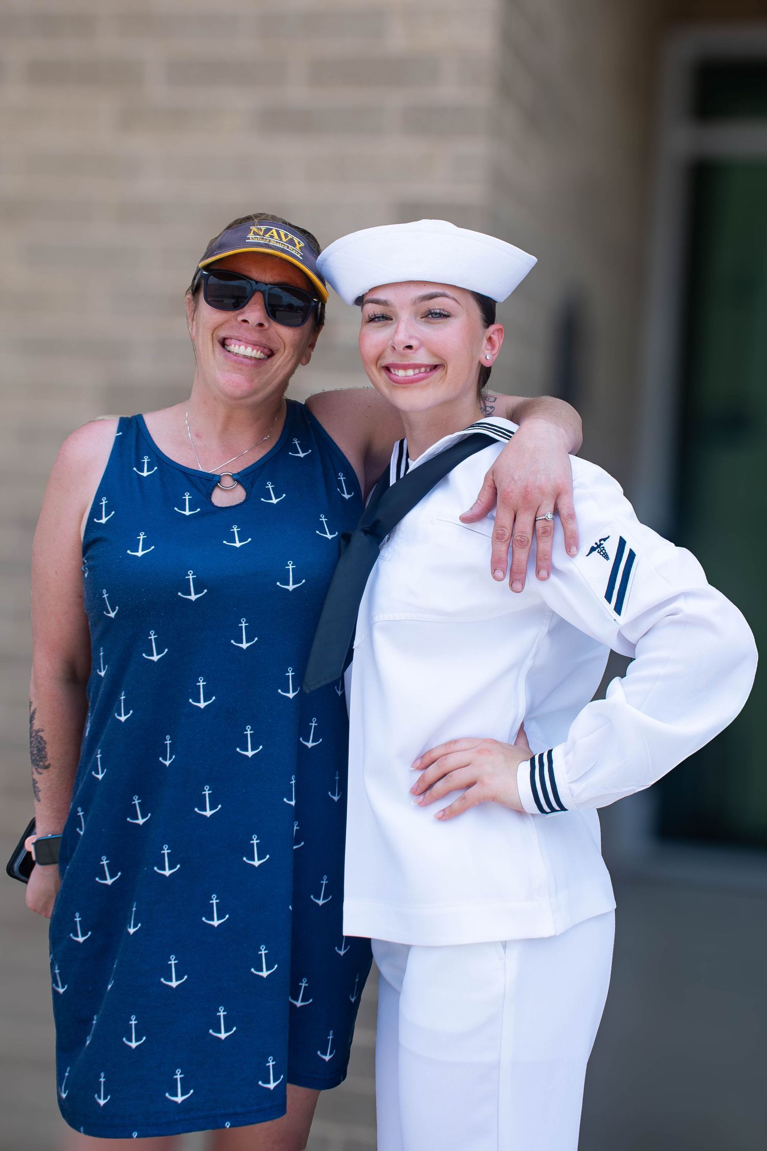 Female US Navy sailor in white uniform and cap posing with a woman in a navy anchor dress.