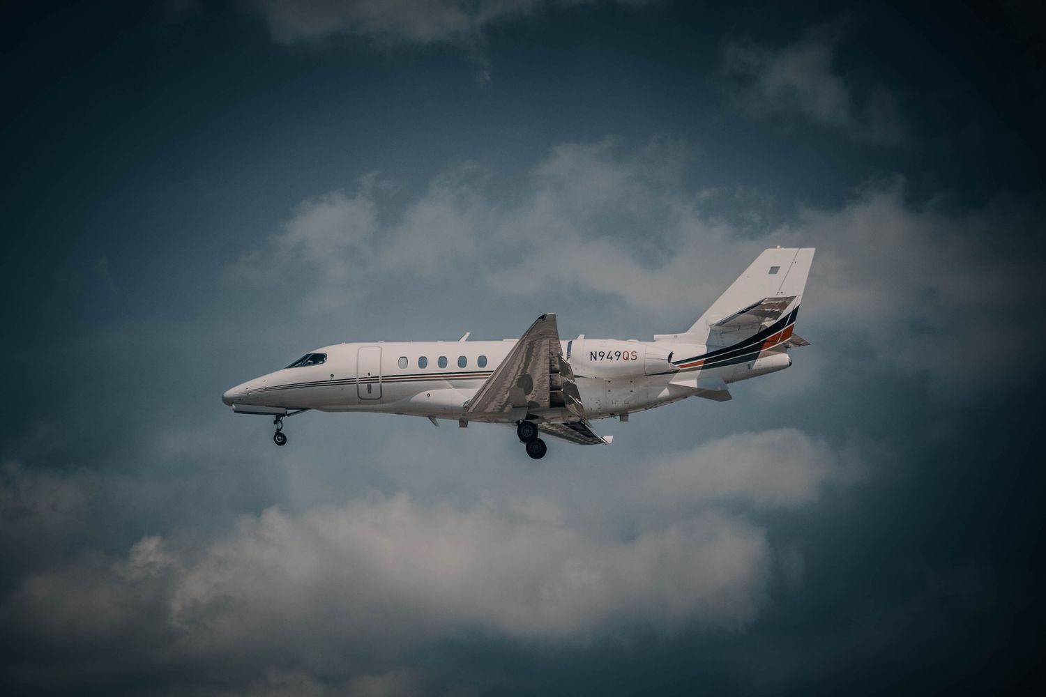 White private jet aircraft flying against dramatic cloudy sky, captured from below during approach or departure.