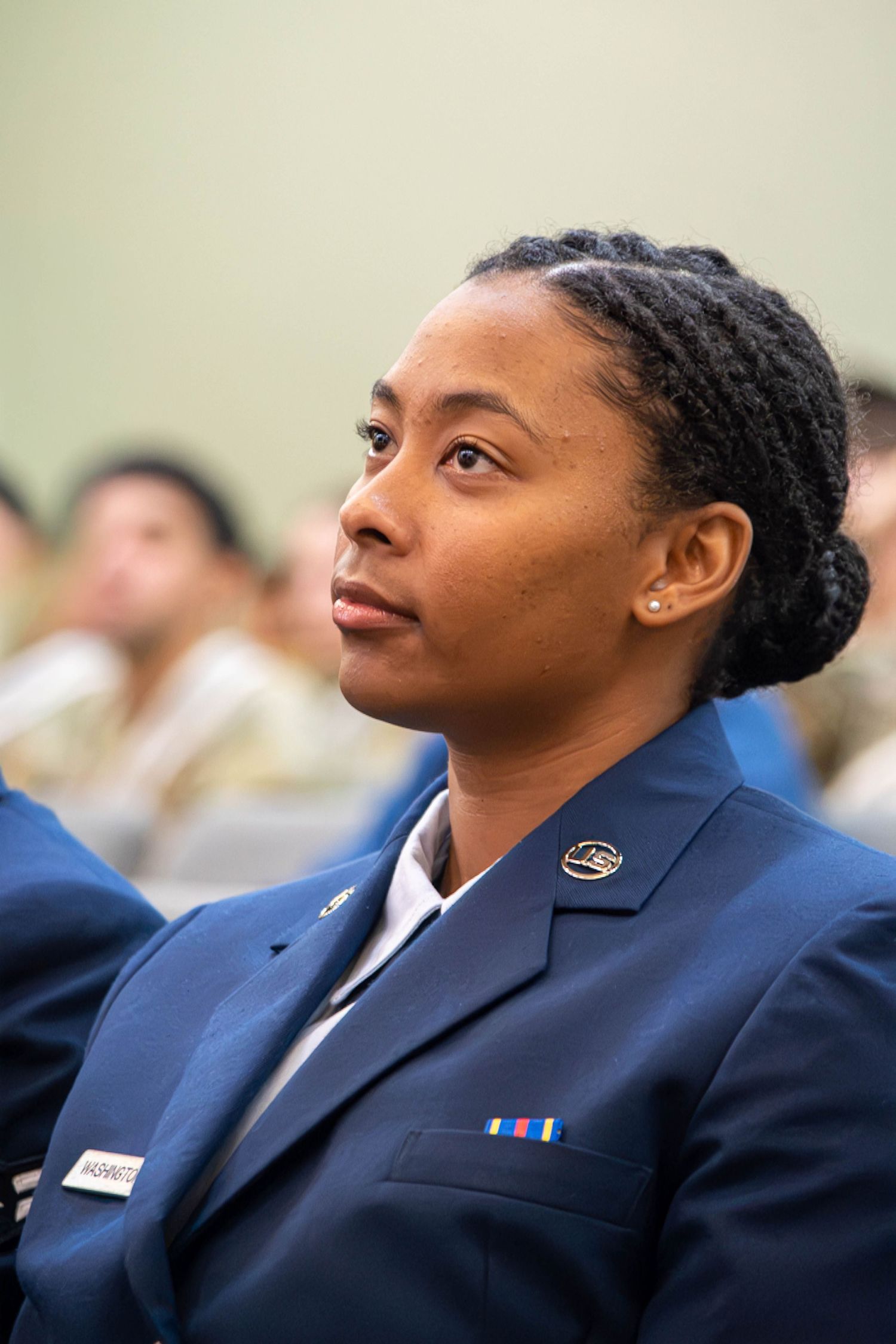 Female Air Force servicewoman in blue dress uniform with ribbon looks attentively forward.