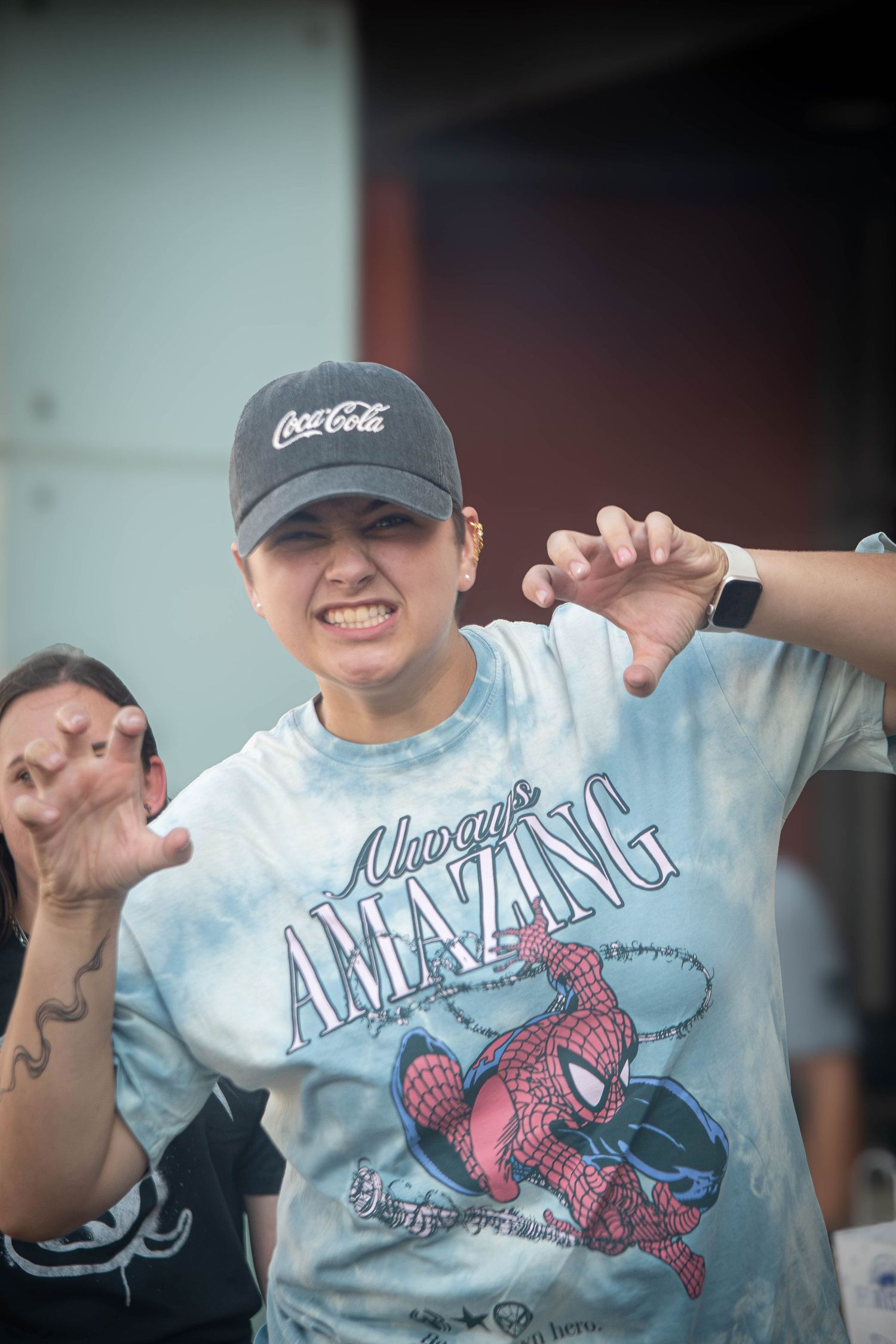 Person wearing Coca-Cola cap and Spider-Man Amazing t-shirt making claws gesture outdoors.