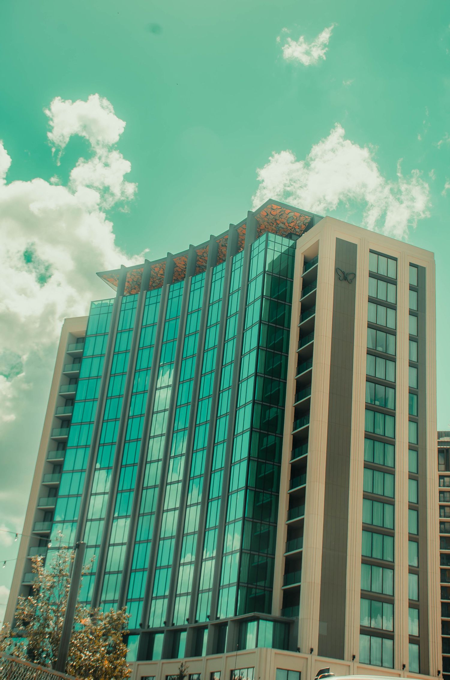 Modern glass office tower with teal reflective windows against a cloudy sky.
