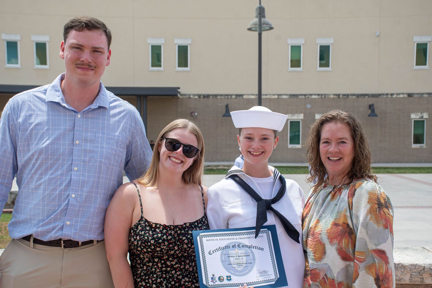 Navy sailor in white uniform poses with family holding Certificate of Completion at graduation.