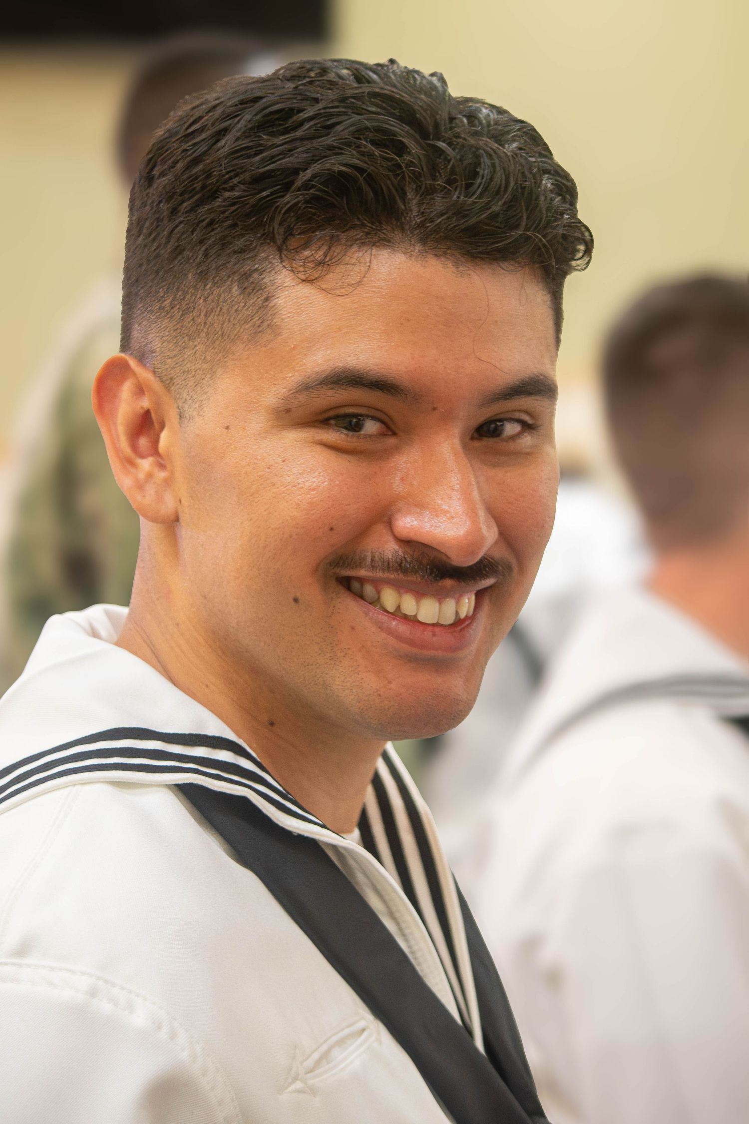 Smiling male U.S. Navy sailor with mustache in white dress uniform at military ceremony.
