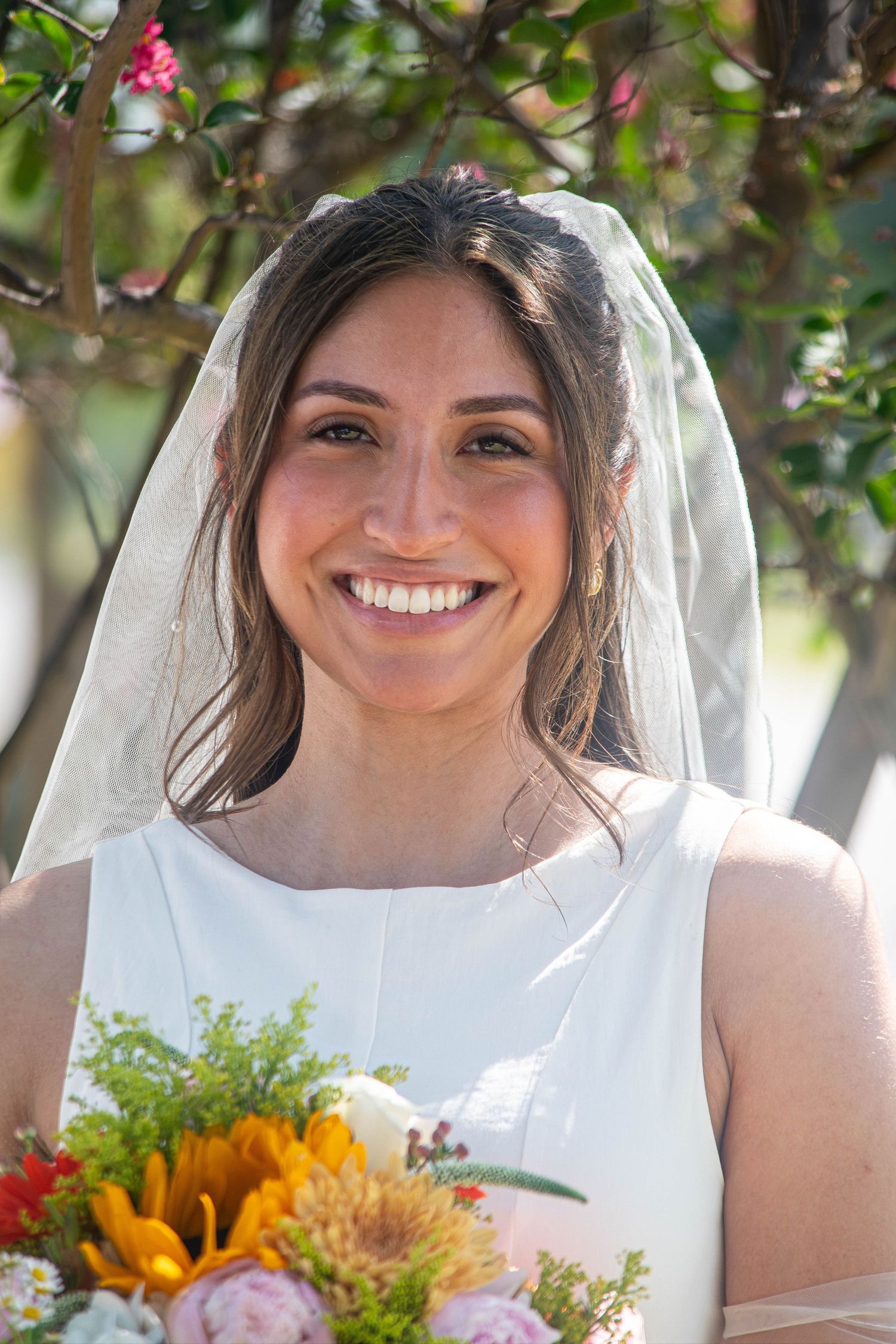Beautiful bride smiling in white dress and veil holding sunflower wedding bouquet outdoors.