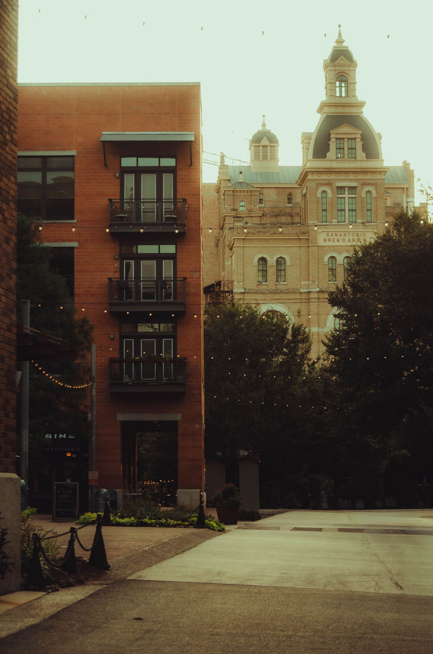 Historic ornate building with dome beside modern red brick building on a quiet urban street.