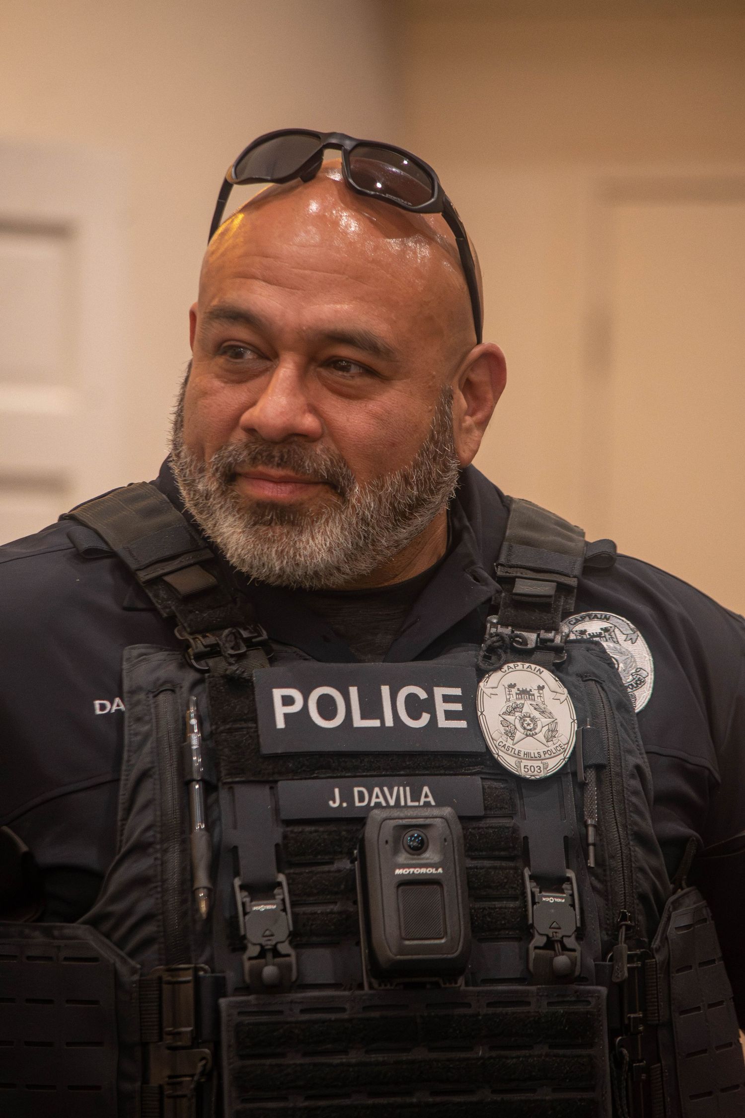 Police officer J. Davila in tactical gear and badge smiling indoors.