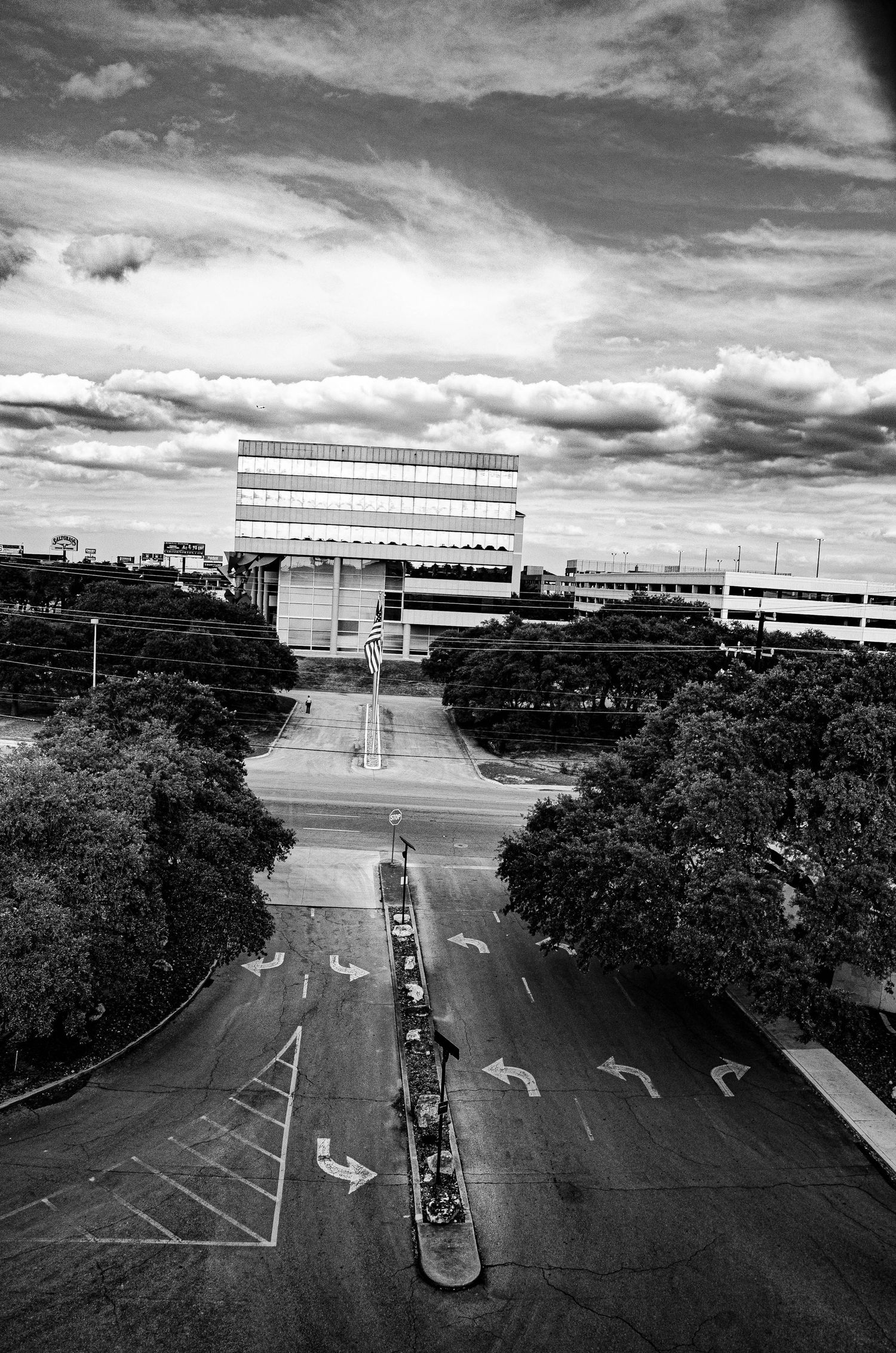 Black and white aerial view of an empty intersection with directional arrows and modern building.
