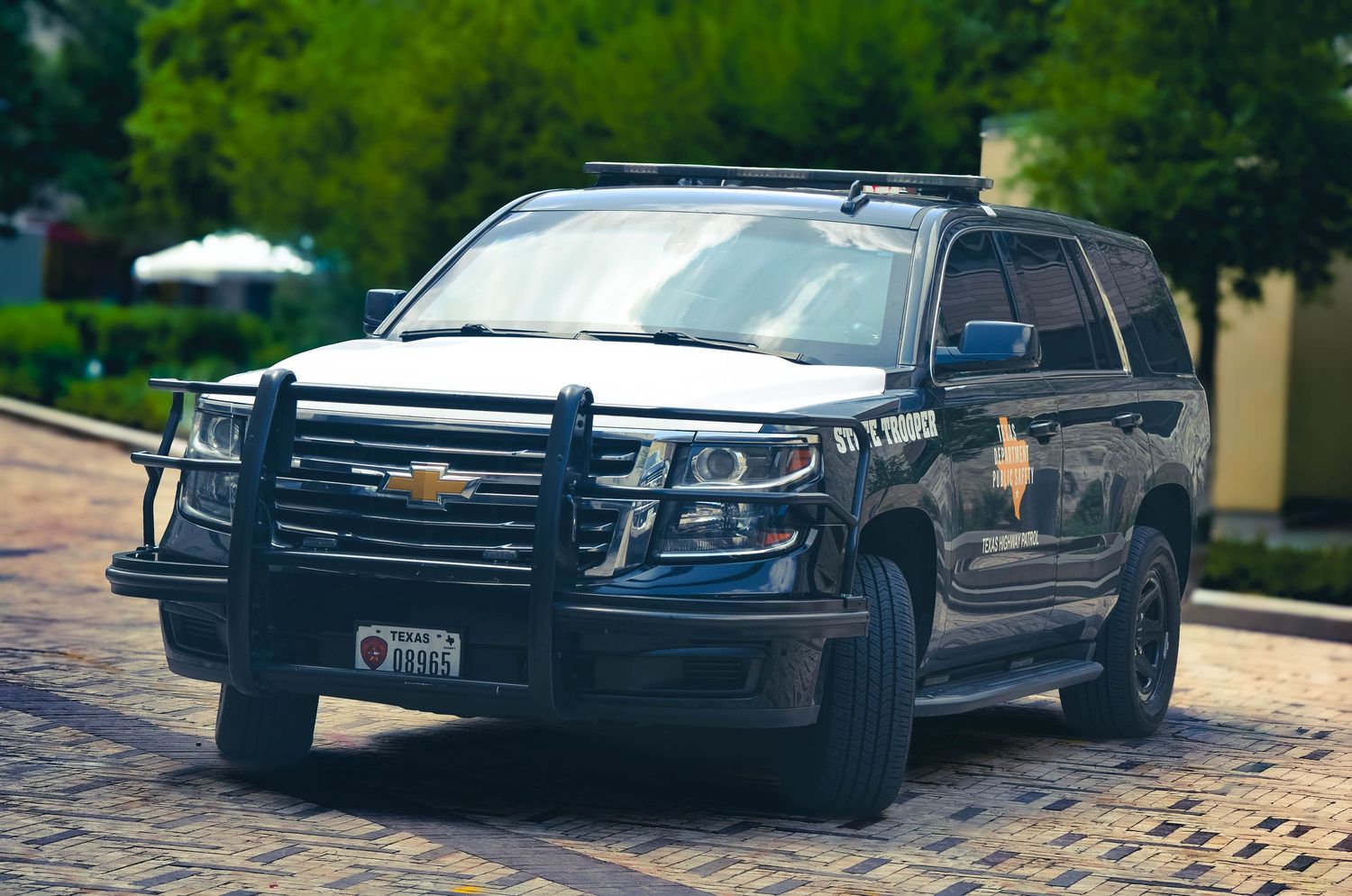Black Chevrolet Tahoe police SUV with roof rack and push bumper parked on brick driveway.