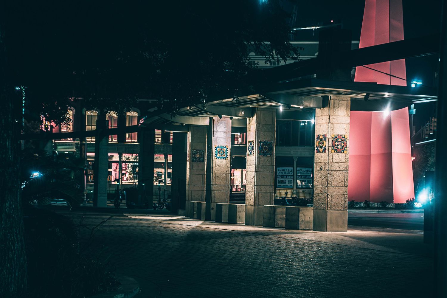 Illuminated urban building exterior with decorative columns and red architectural accent at night.