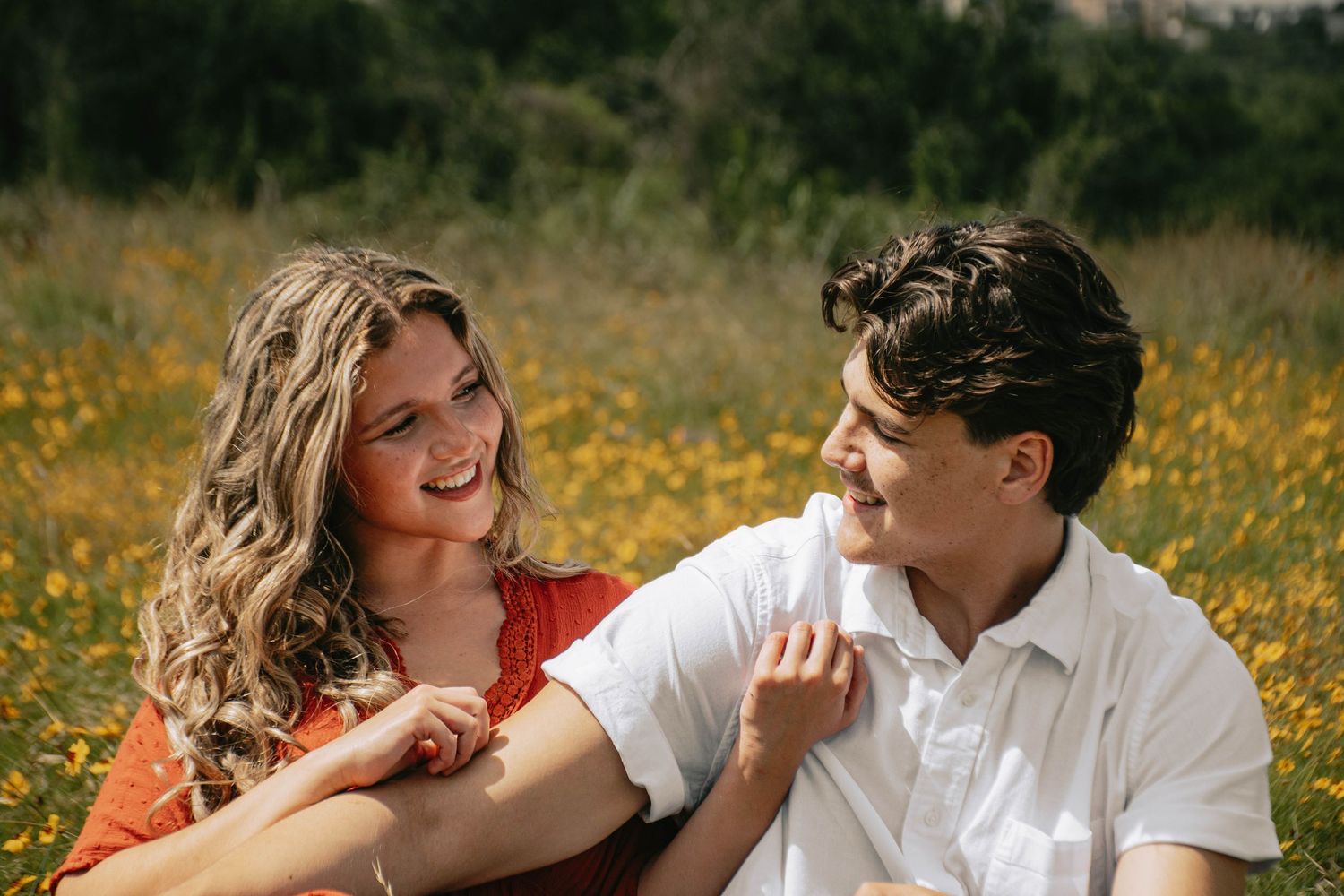 Smiling couple sitting together in a yellow wildflower meadow on a sunny day.