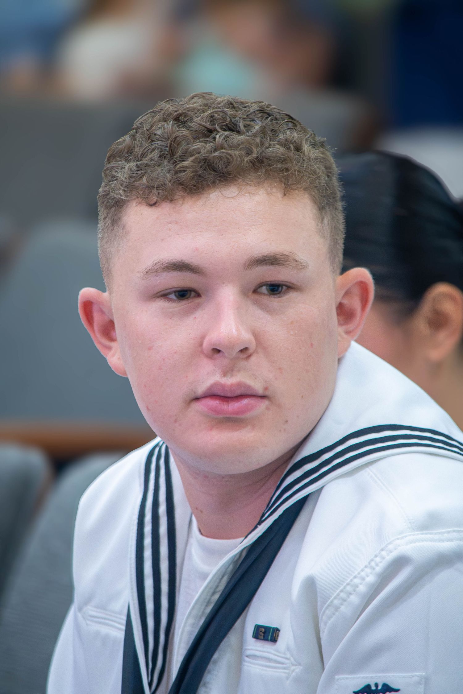 Young male US Navy sailor in white uniform with a serious expression.