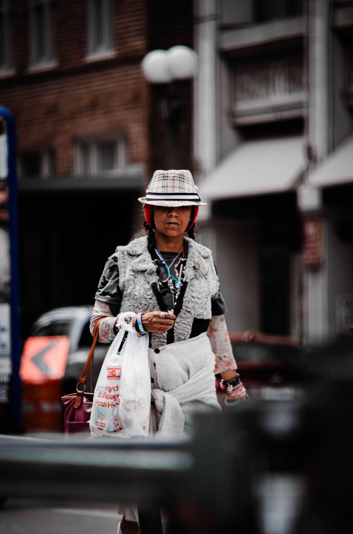 Elderly Asian woman in stylish hat and fur jacket carrying shopping bags on a city street.