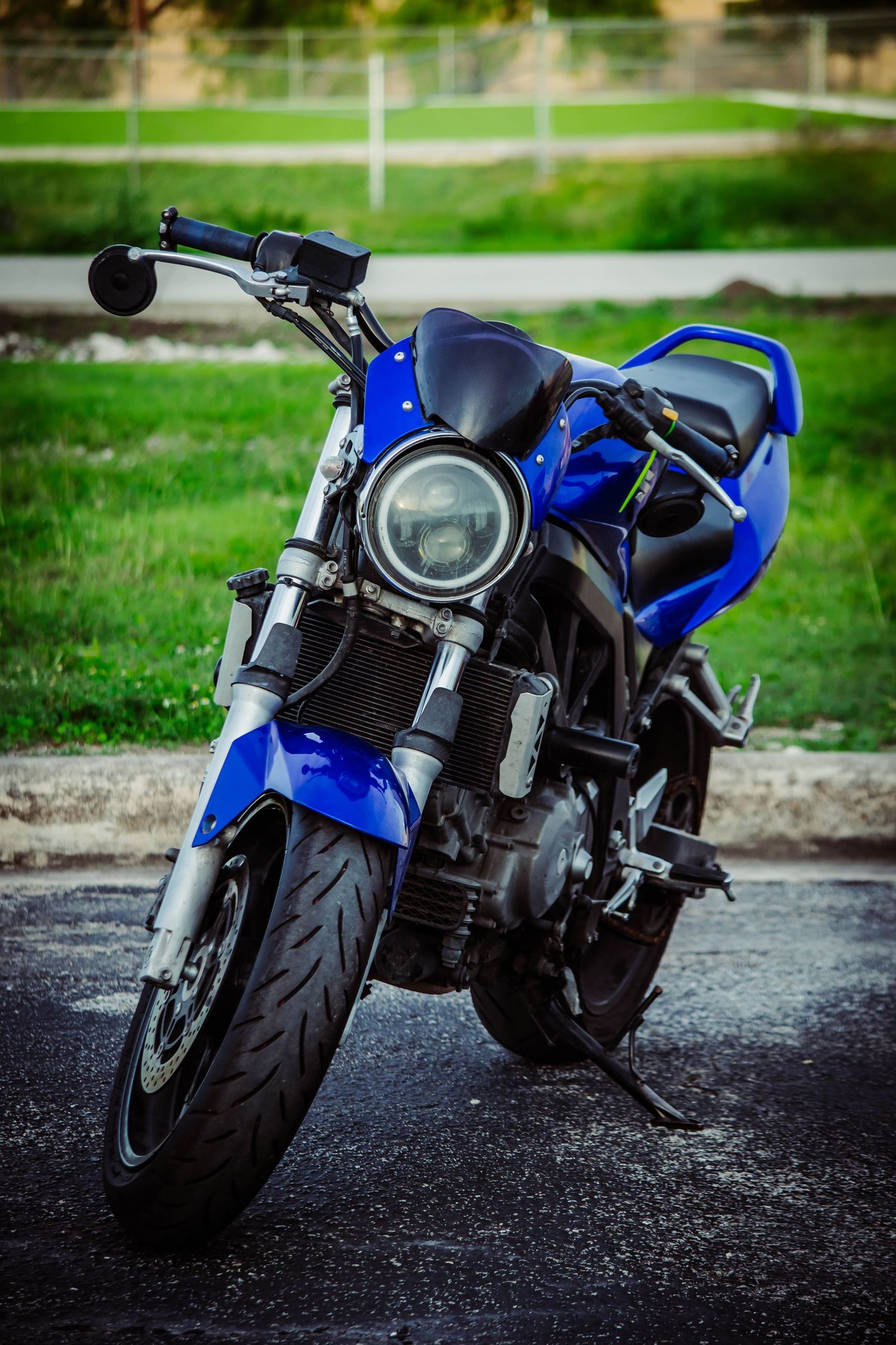 A sleek blue and black sport motorcycle parked on asphalt with a green grassy background.