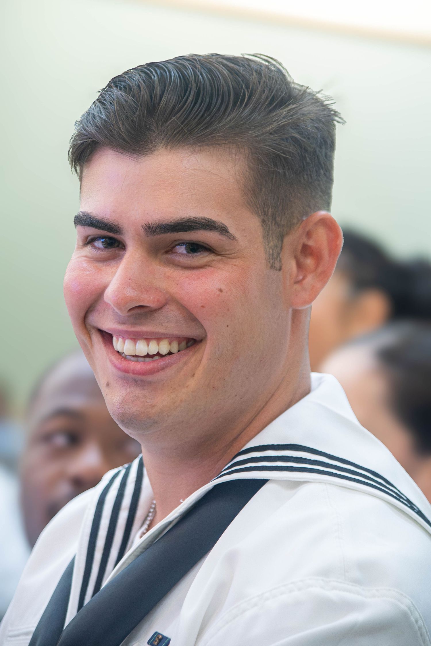 Smiling young male US Navy sailor in white uniform at a military ceremony.