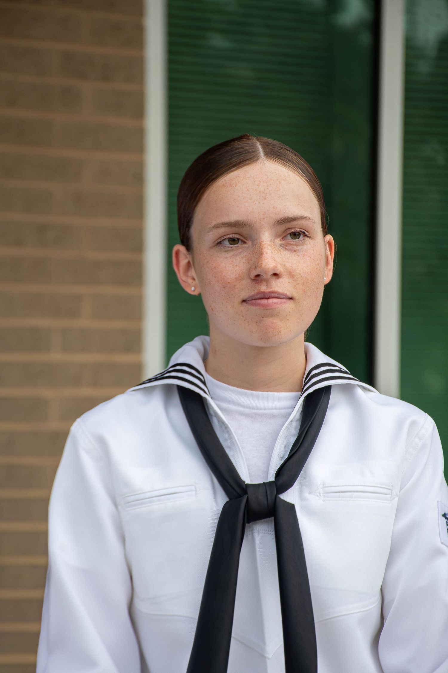 Young female Navy sailor in dress whites uniform poses outside a brick building.