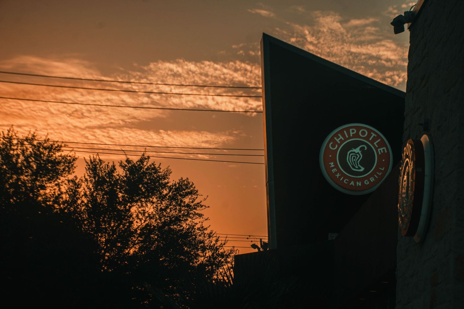 Chipotle Mexican Grill sign silhouetted against a vivid orange sunset sky.