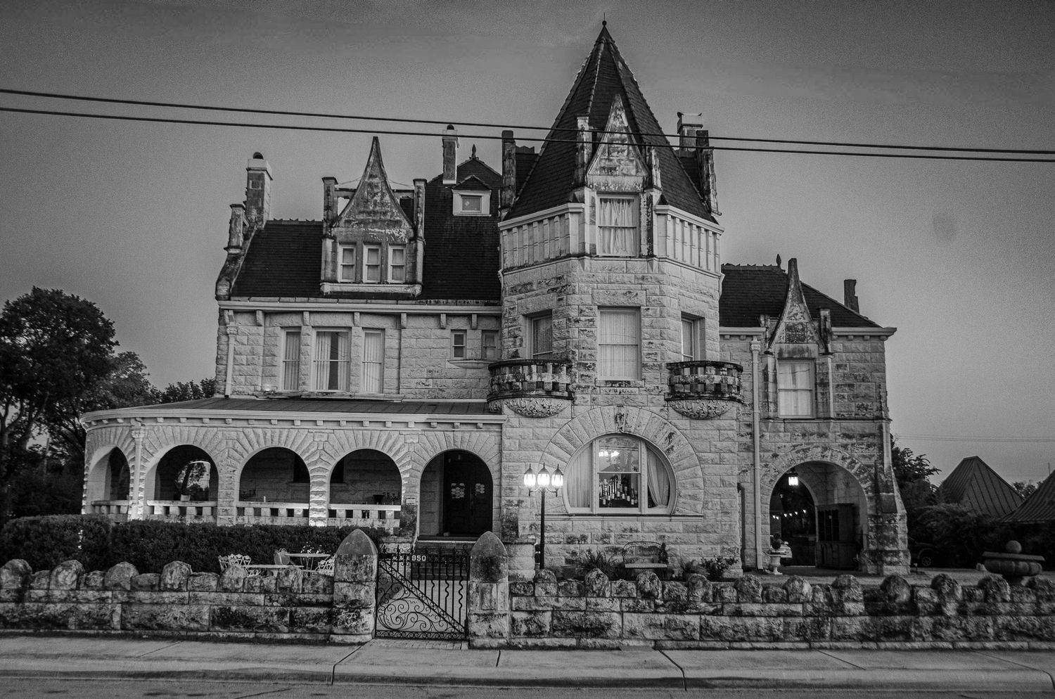 Gothic Victorian mansion with stone facade and ornate architecture photographed in black and white at dusk.