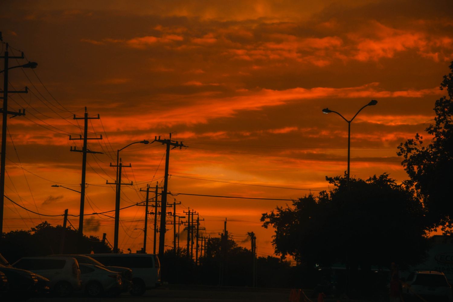 Dramatic red and orange sunset sky over silhouetted utility poles and trees lining a suburban street.