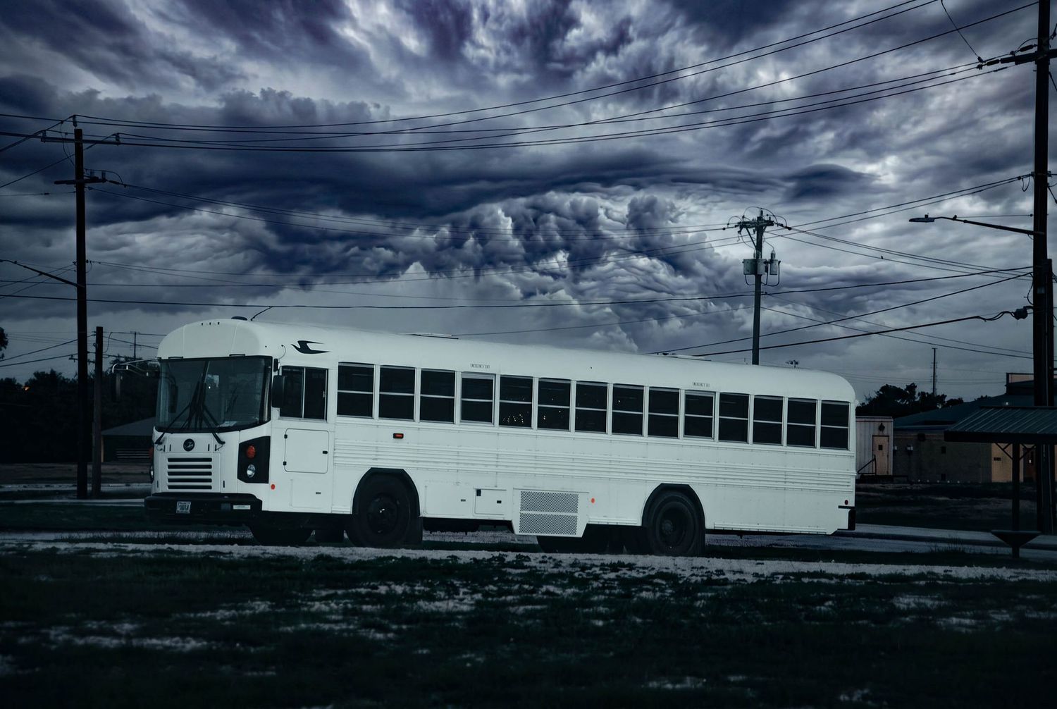 White school bus parked under dramatic stormy sky with dark clouds, moody atmospheric outdoor scene.