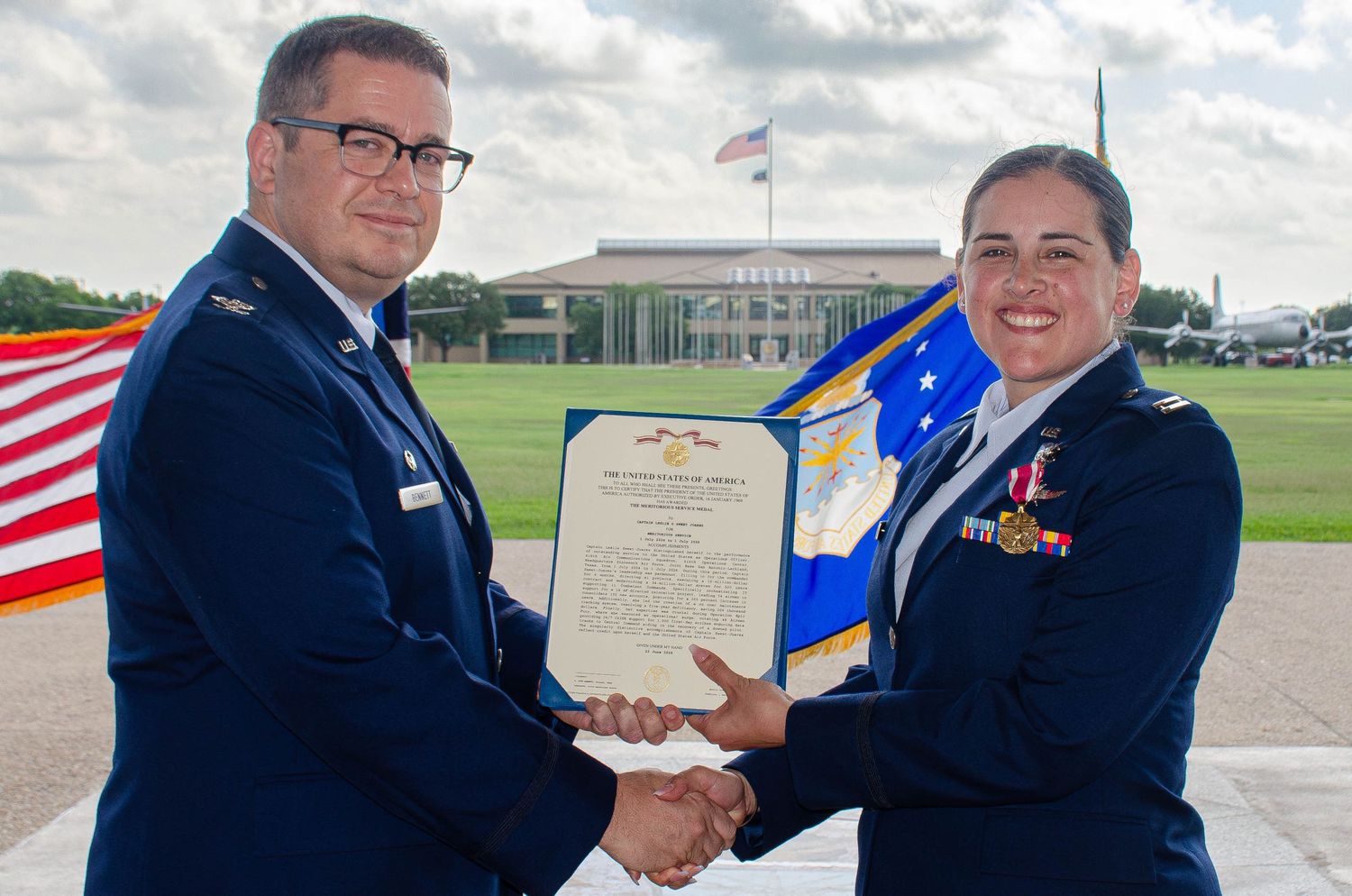 US Air Force officer shaking hands with a female airman while presenting an official certificate.