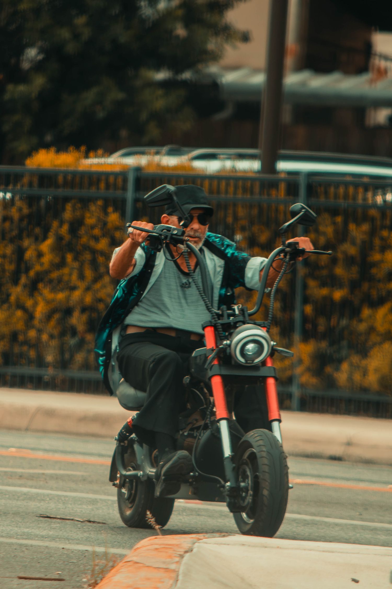 A man riding a small electric motorcycle on a city street with autumn foliage in the background.