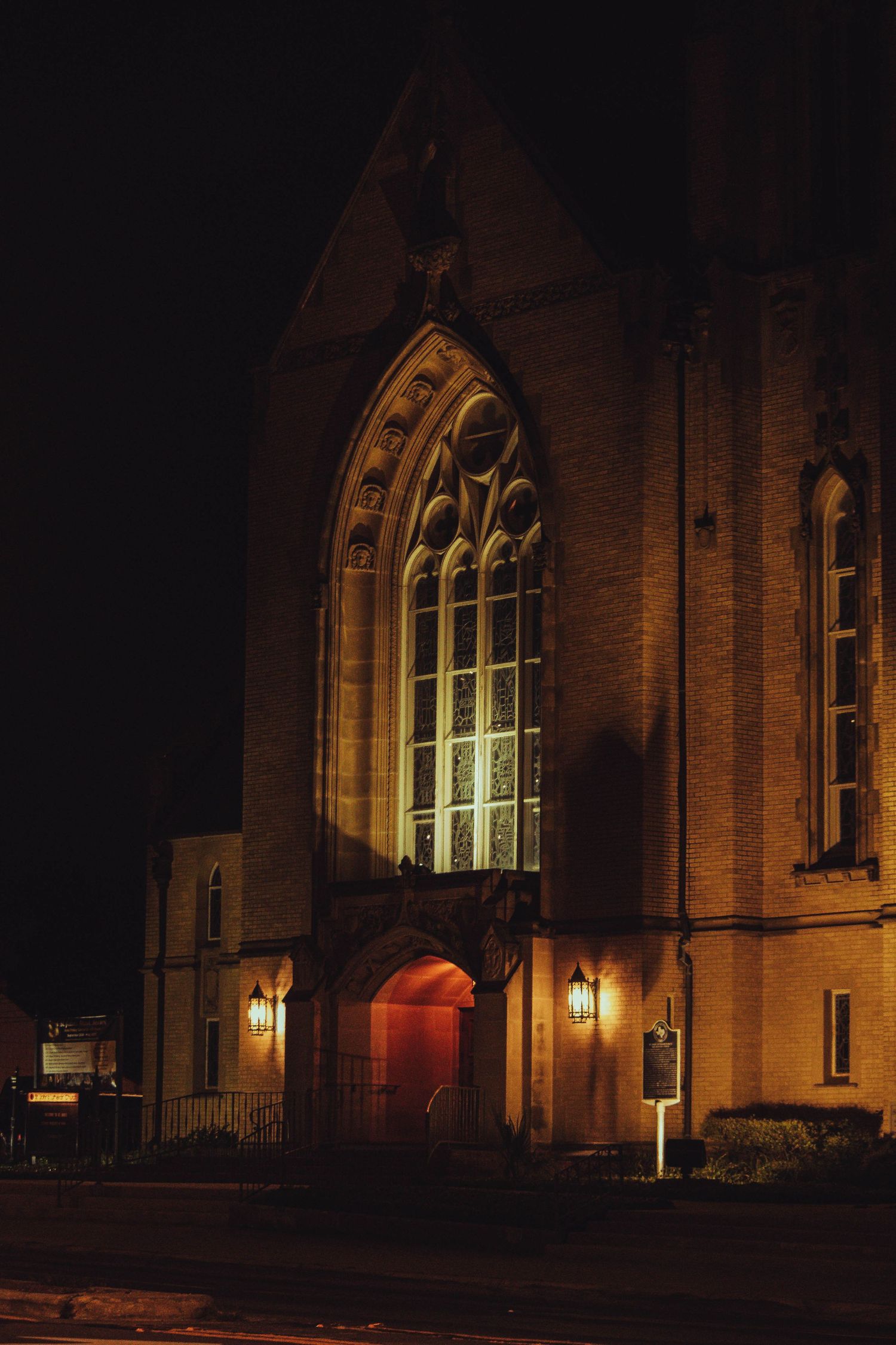 Gothic church illuminated at night with warm lights highlighting arched windows and entrance doors.