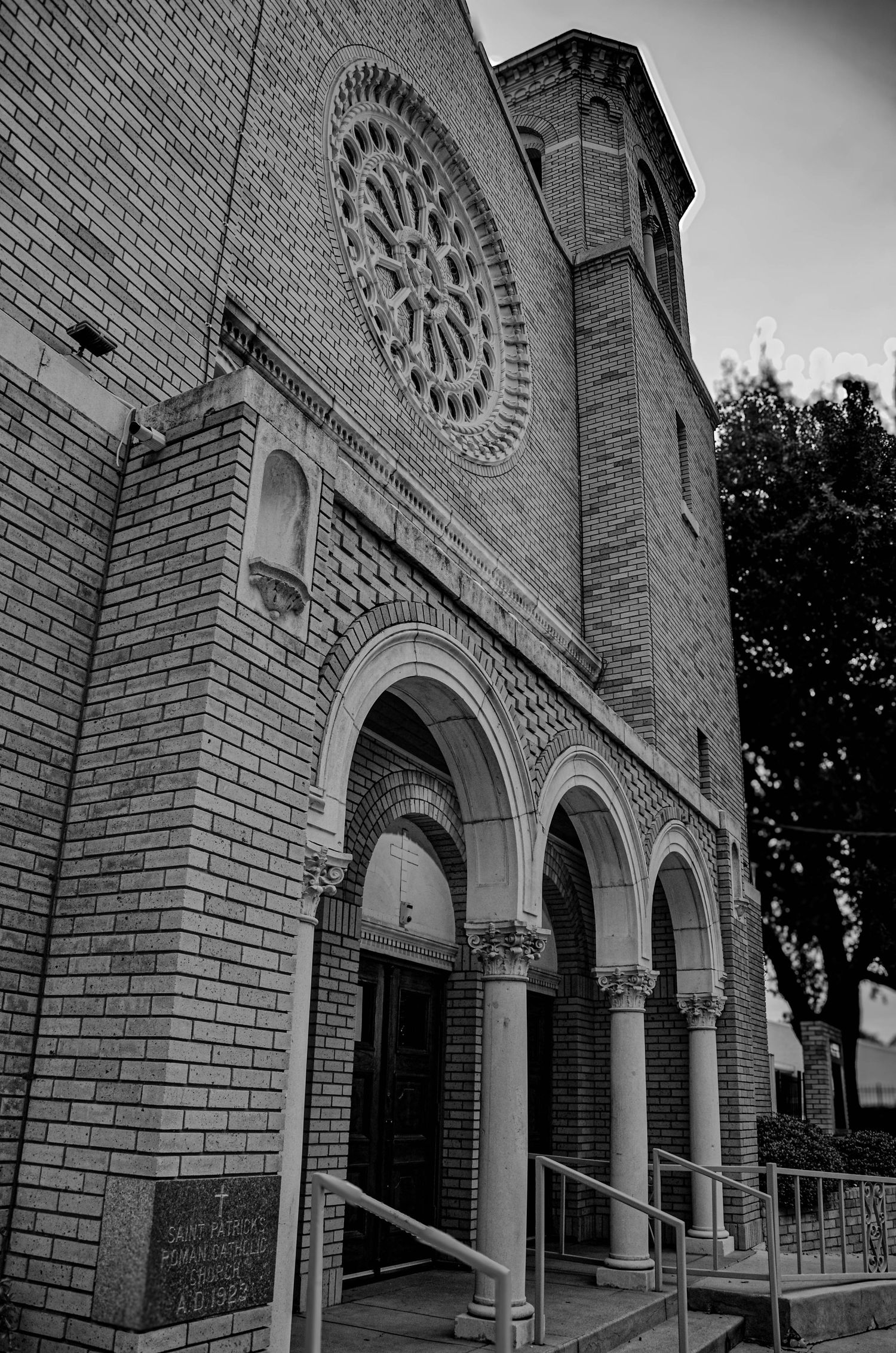 Black and white photo of a historic brick Catholic church facade with arched entrance and rose window.