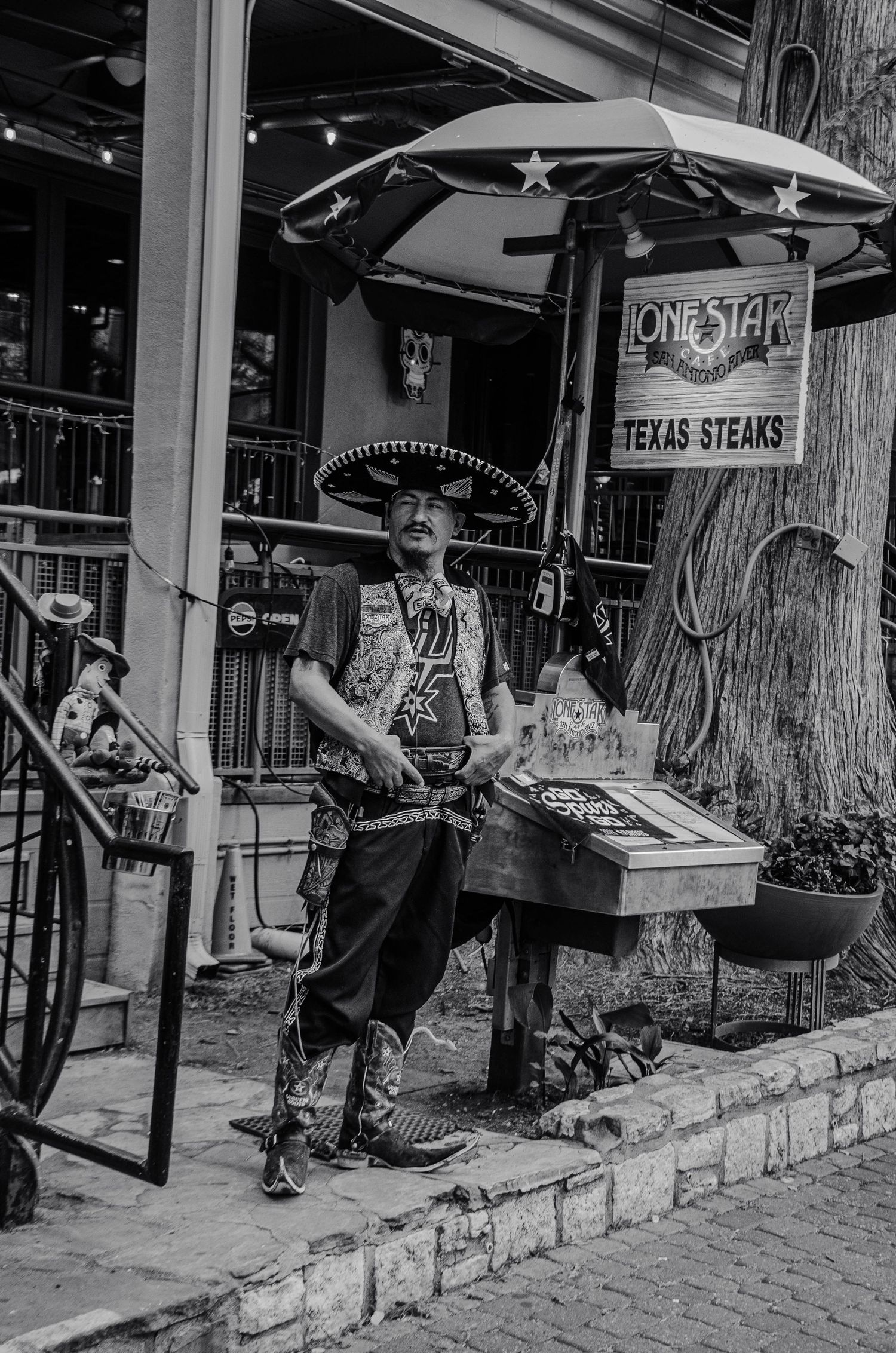 Street performer in sombrero and cowboy attire outside Lone Star Texas Steaks in black and white.